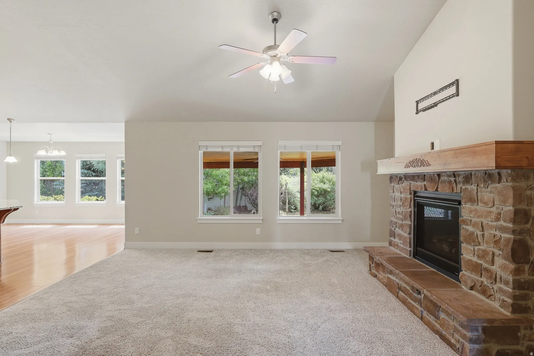 VBright family room with large windows, a stone fireplace, vaulted ceilings and a ceiling fan.