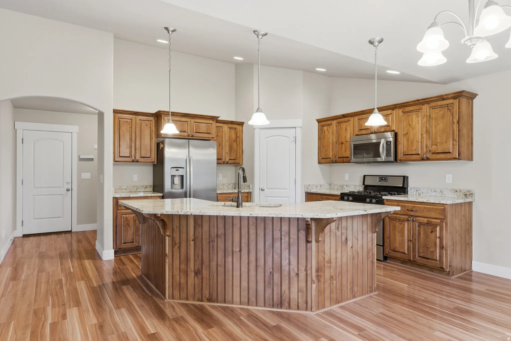 Gourmet kitchen featuring a central island with integrated sink, custom Alder cabinetry, stainless steel appliances, granite countertops, and hardwood flooring.