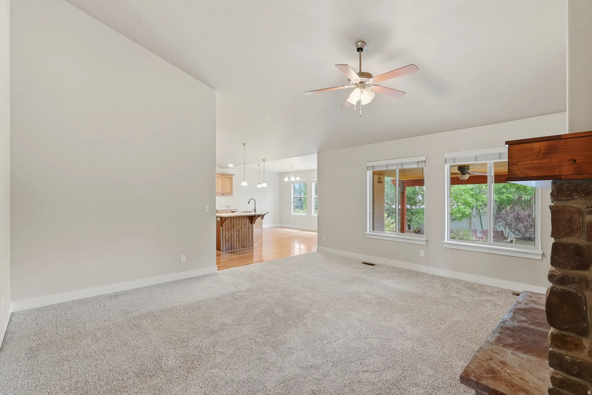 Bright family room with large windows, a stone fireplace, vaulted ceilings and a ceiling fan.