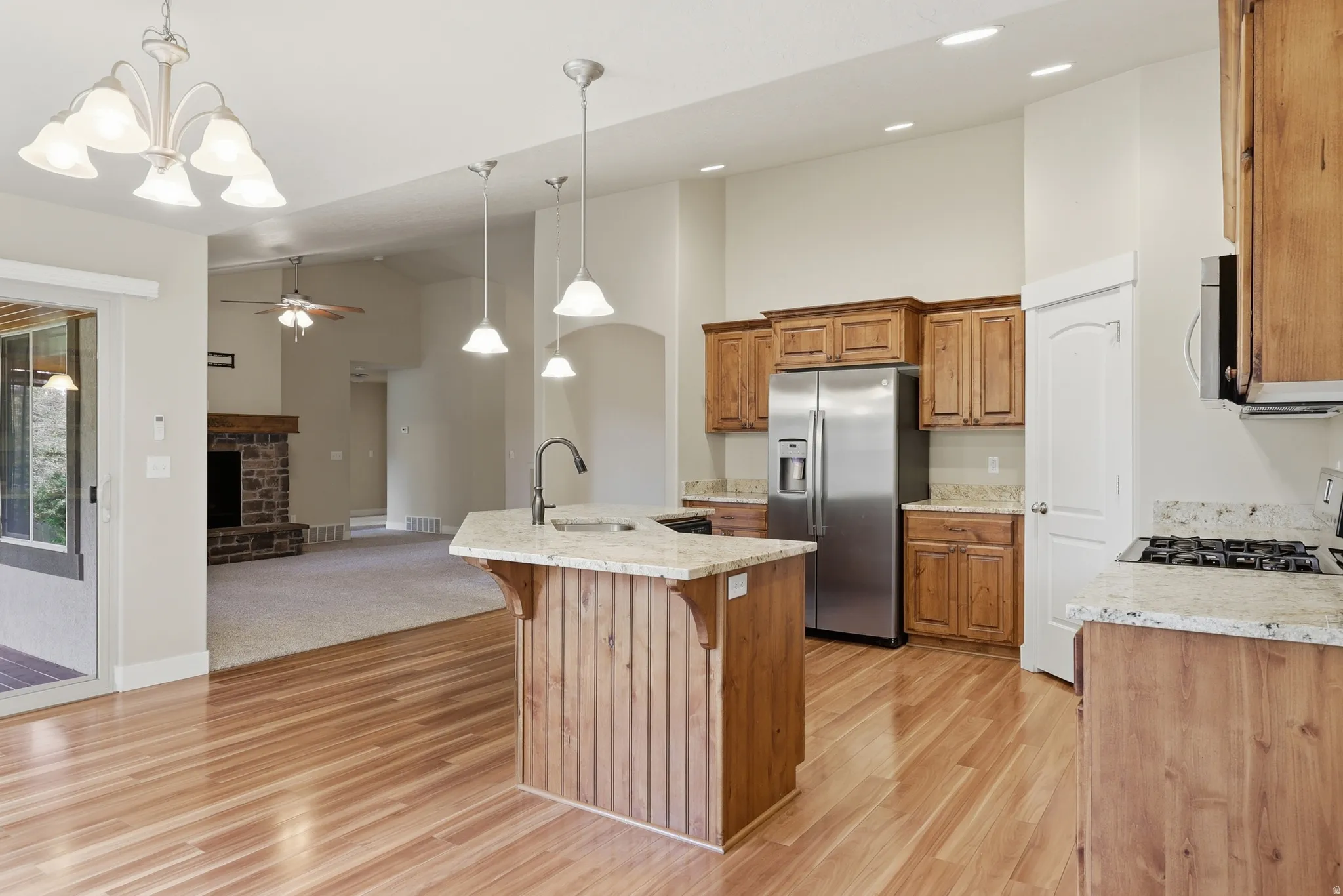 Gourmet kitchen featuring a central island with integrated sink, custom Alder cabinetry, stainless steel appliances, granite countertops, and hardwood flooring.