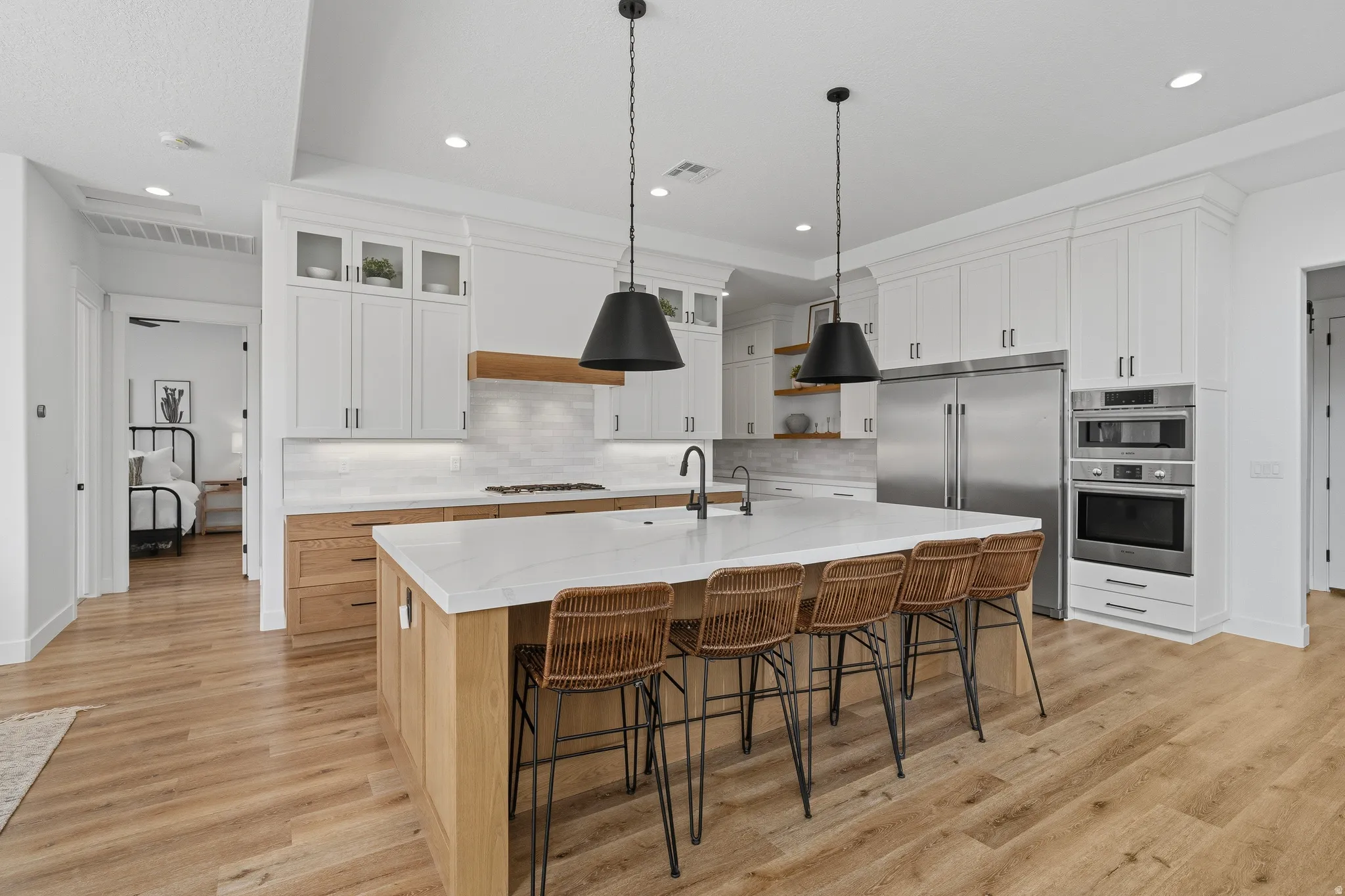 Spacious kitchen featuring a large central island with seating, light wood-finish flooring, white upper cabinetry, natural wood lower cabinetry, and stainless steel appliances.