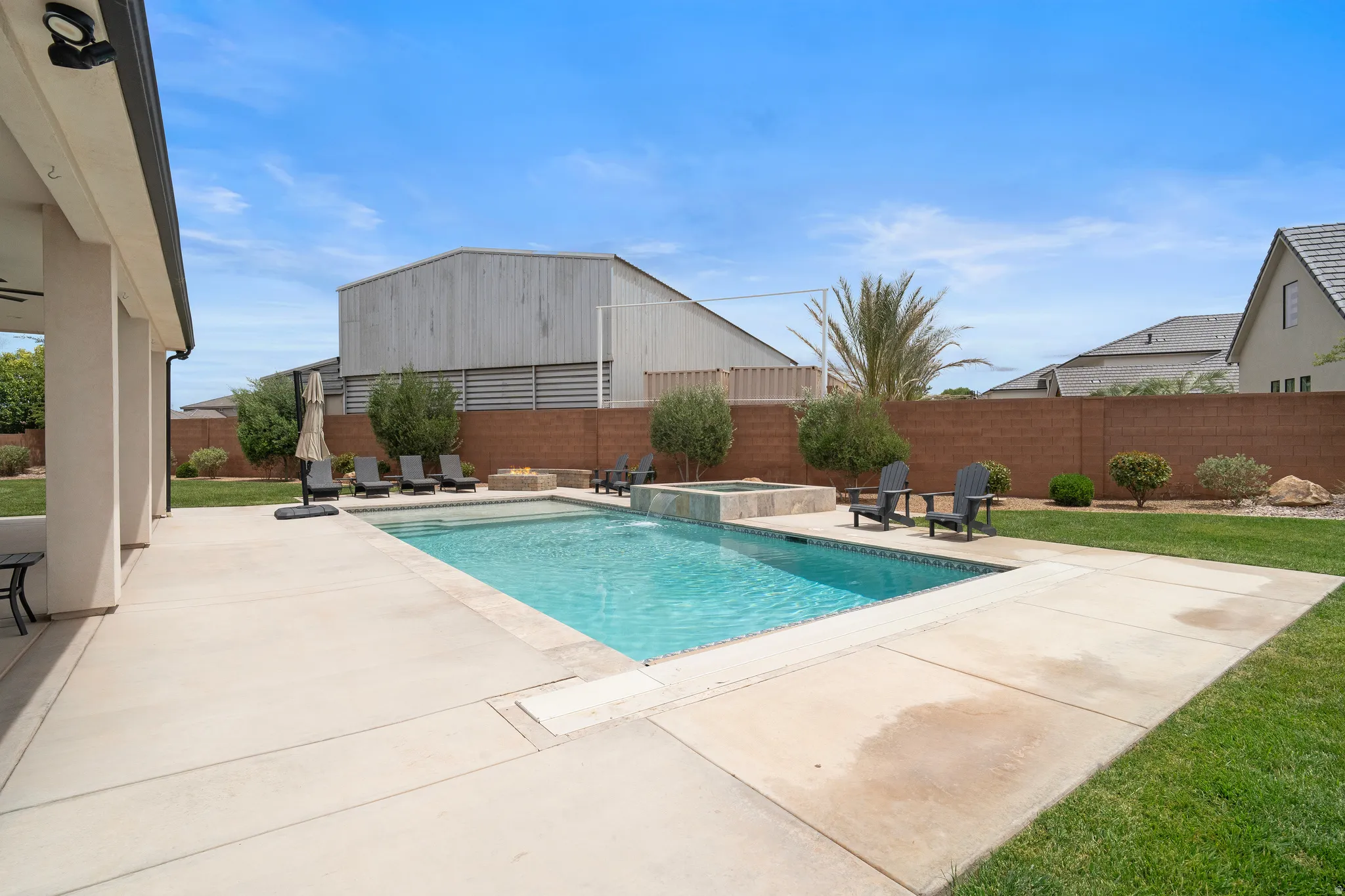 Expansive backyard featuring a rectangular swimming pool, integrated spa, fire pit, and mature perimeter landscaping.
