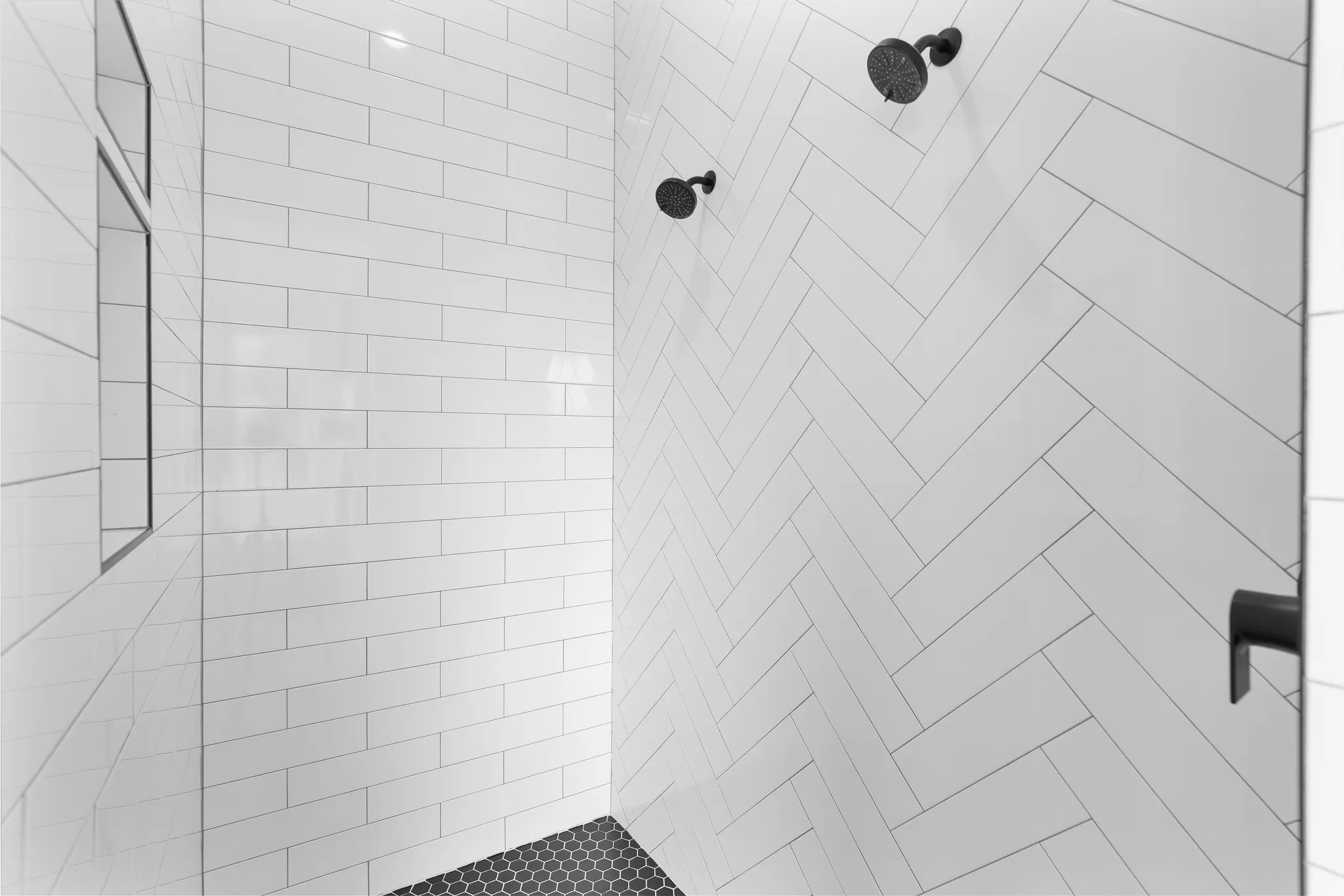 Shower with white subway tile in a herringbone pattern, matte black fixtures, and a black hexagonal tile floor.