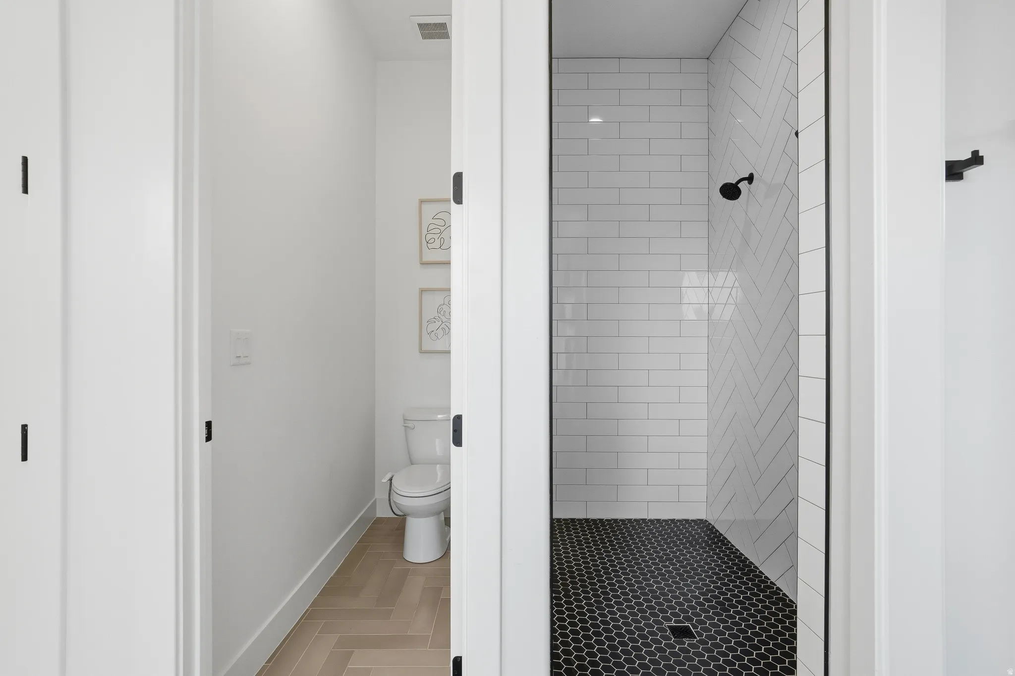 Contemporary shower stall featuring white subway tile in a herringbone pattern, a black hexagonal tile floor, and a matte black shower head.