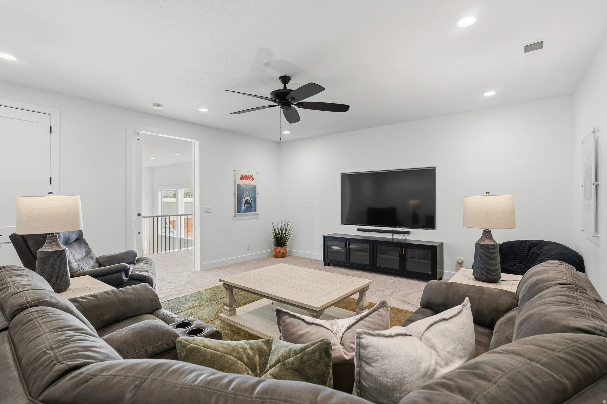 Spacious media room featuring recessed lighting, a ceiling fan, light-colored carpeting, a wall-mounted television, and a media console with glass-front cabinets.