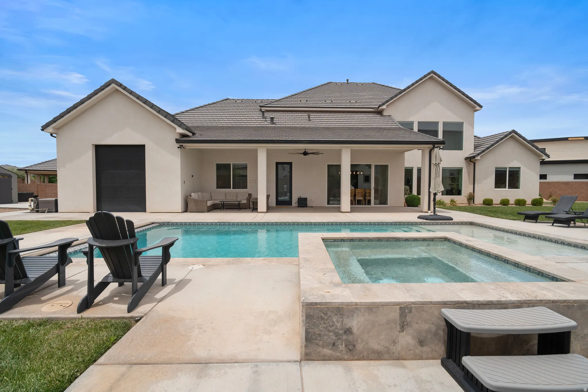 Expansive backyard featuring a rectangular swimming pool, an integrated spa with stone surround, a covered patio with recessed lighting, and a stucco exterior.