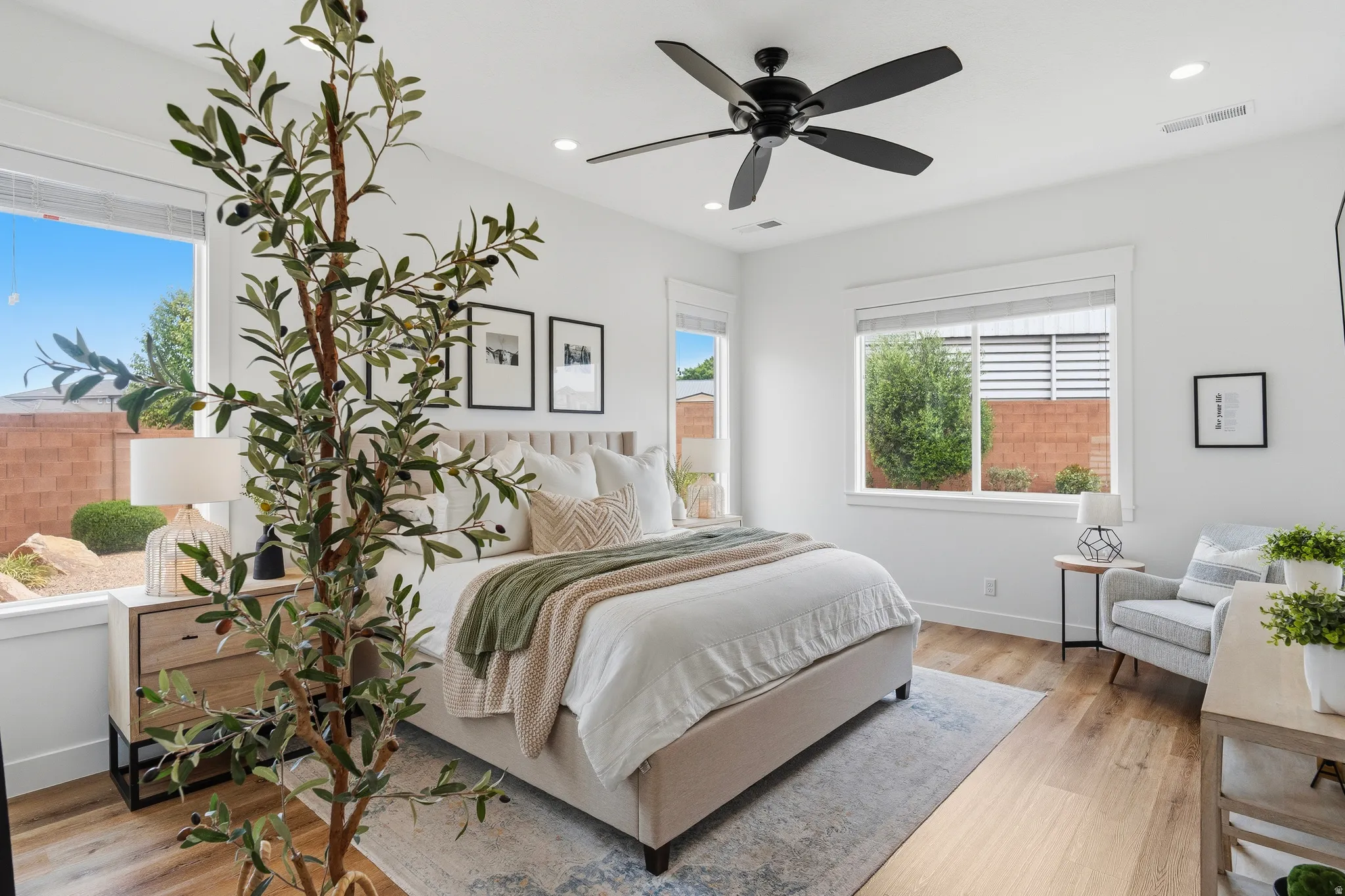 Spacious bedroom featuring light wood-finish flooring, multiple large windows, recessed lighting, and a ceiling fan.