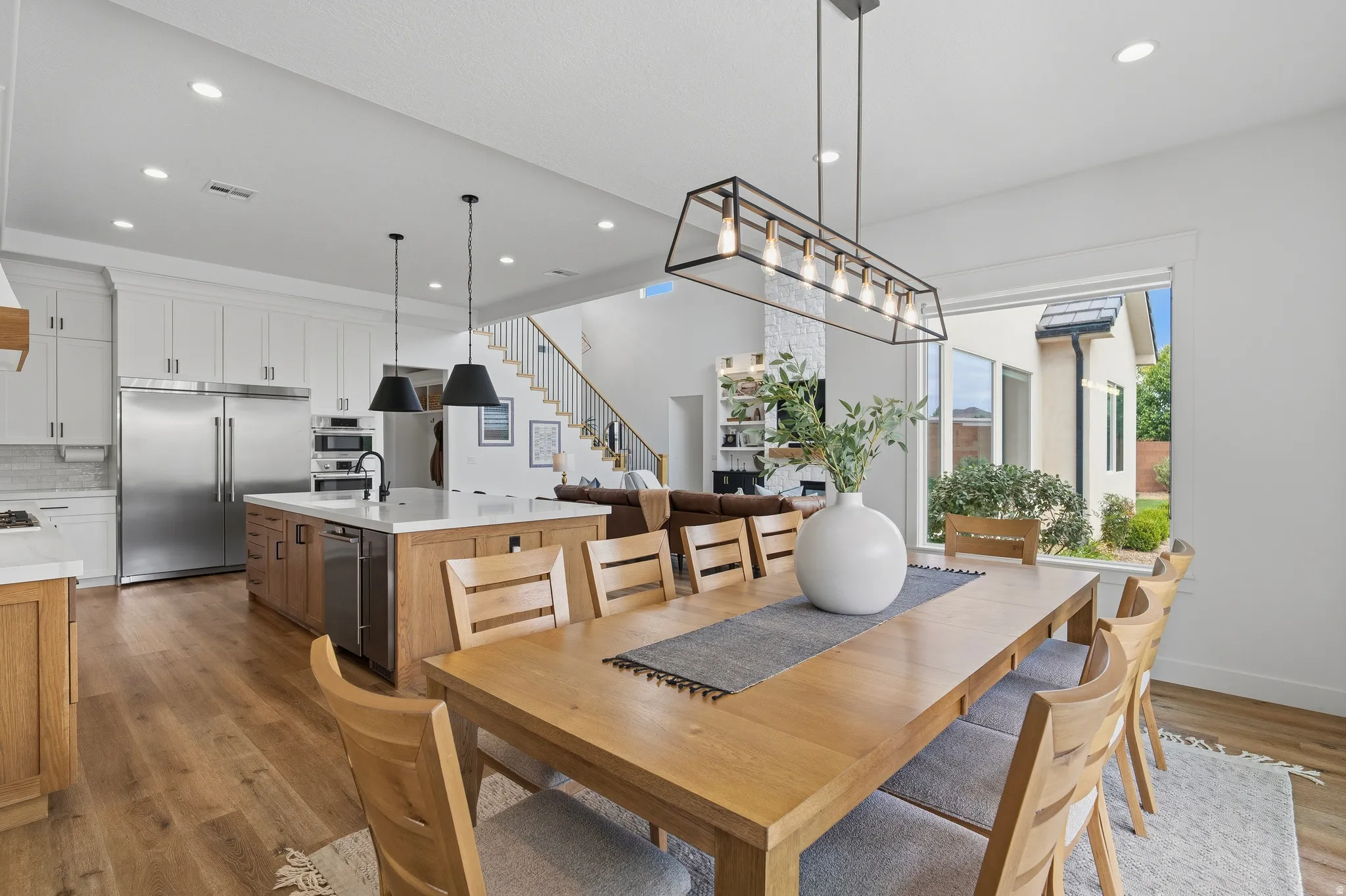 Open-concept dining area with wood-finish flooring and a contemporary linear chandelier.