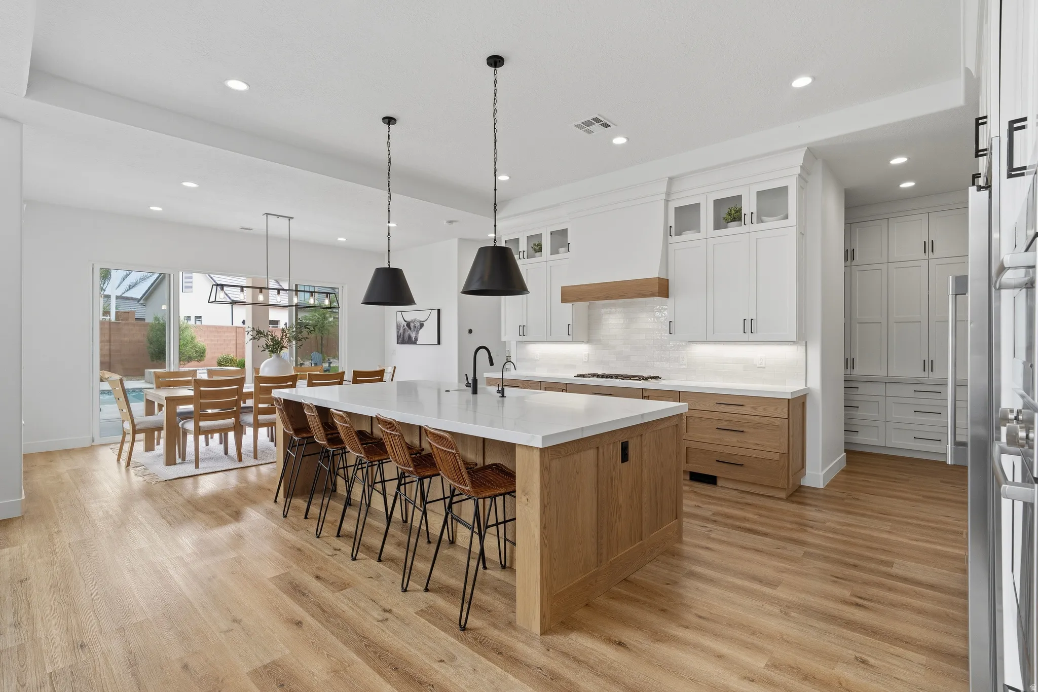Open-concept kitchen featuring a large central island with seating, stone countertops, wood-finish flooring, white upper cabinetry, and wood-finish lower cabinetry.
