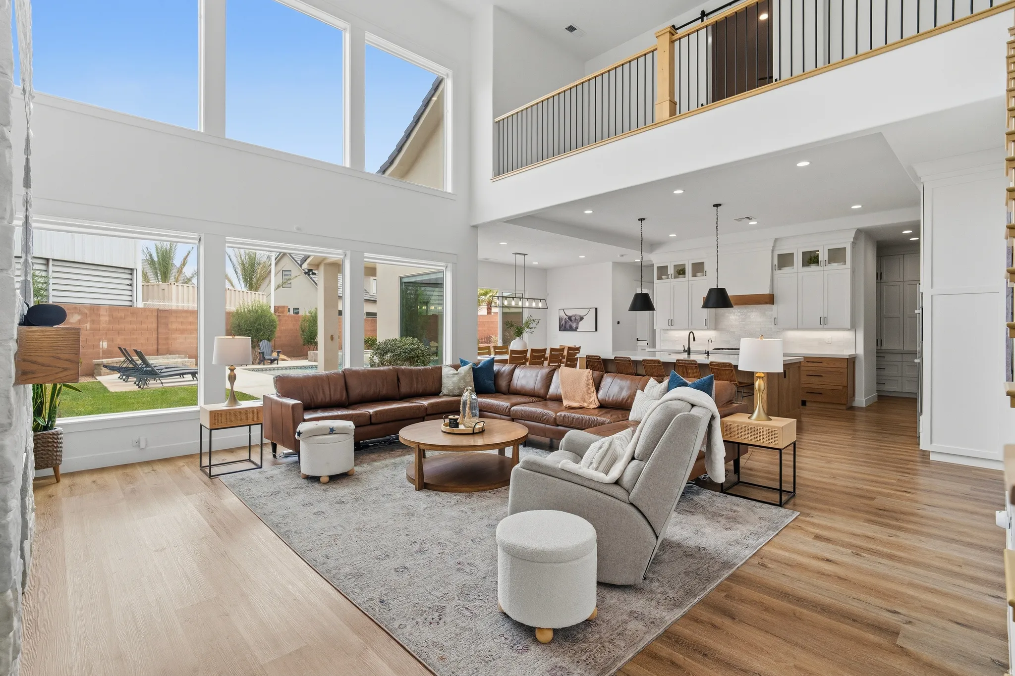 Double-height living space featuring expansive windows, wood-finish flooring, and a modern kitchen with pendant lighting and built-in cabinetry.