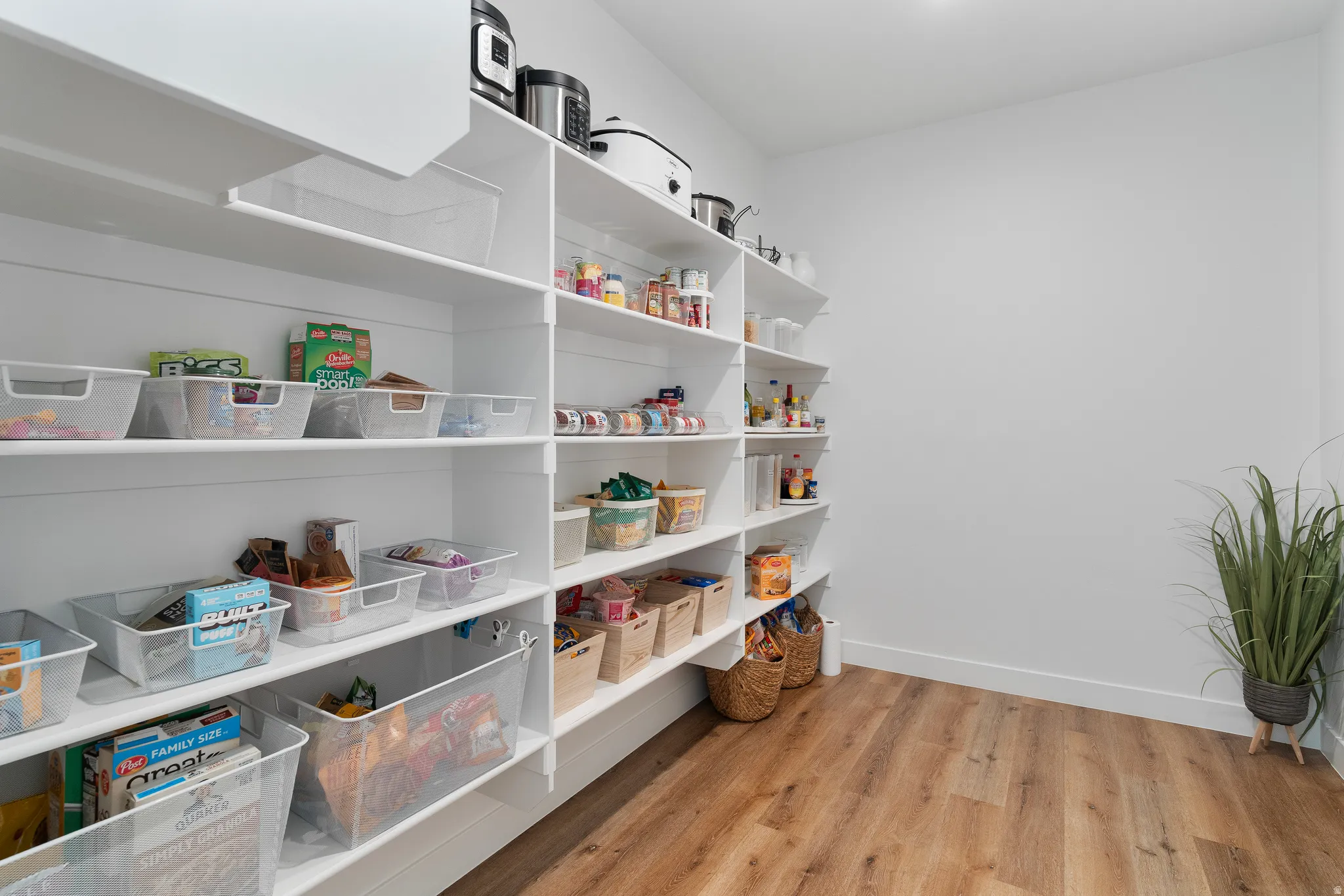 Walk-in pantry featuring extensive white shelving, wood-finish flooring, and recessed ceiling lighting.