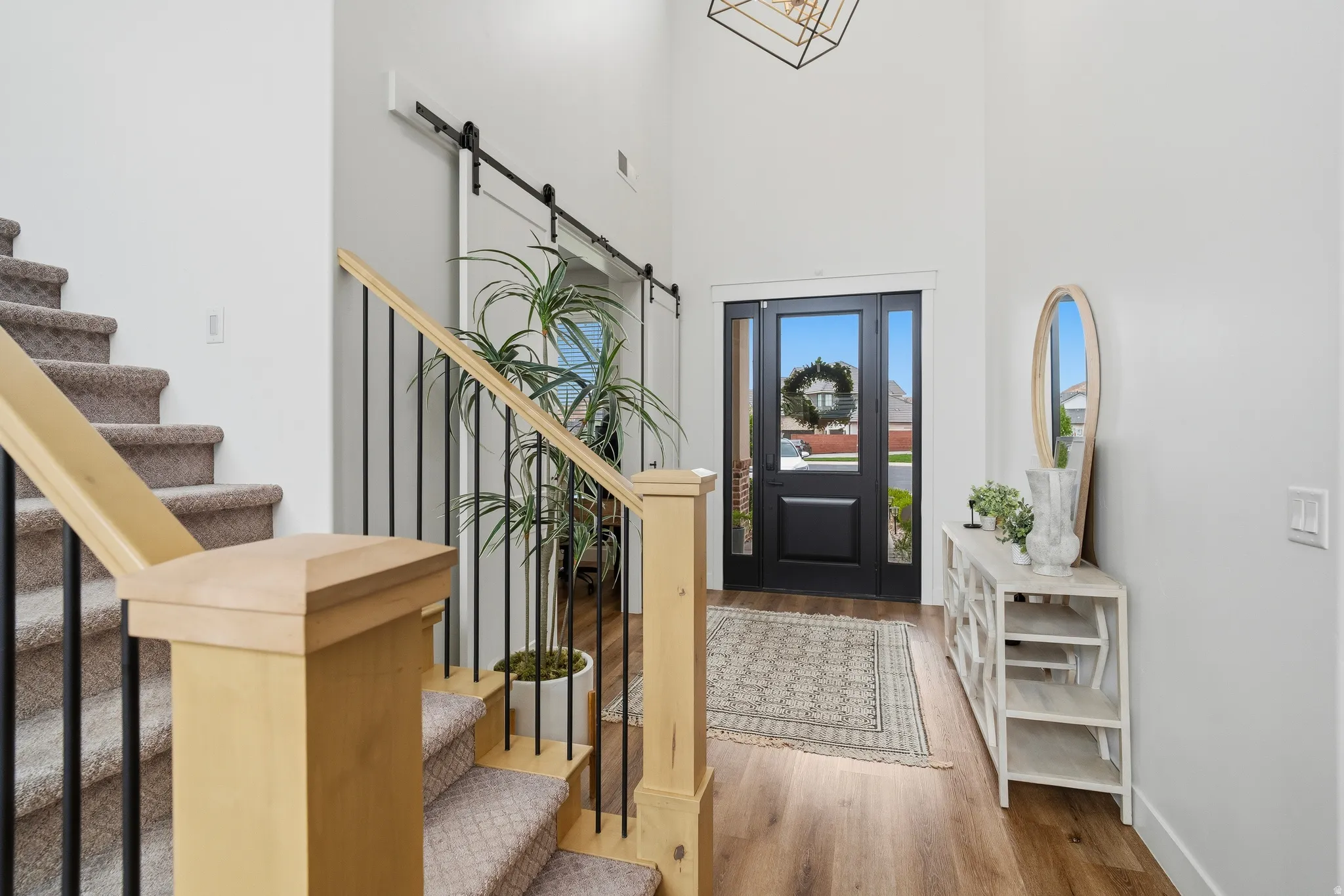 Foyer featuring a tall ceiling, wood-finish flooring, a dark entry door with glass panels, and a contrasting light wood staircase with black metal balusters.