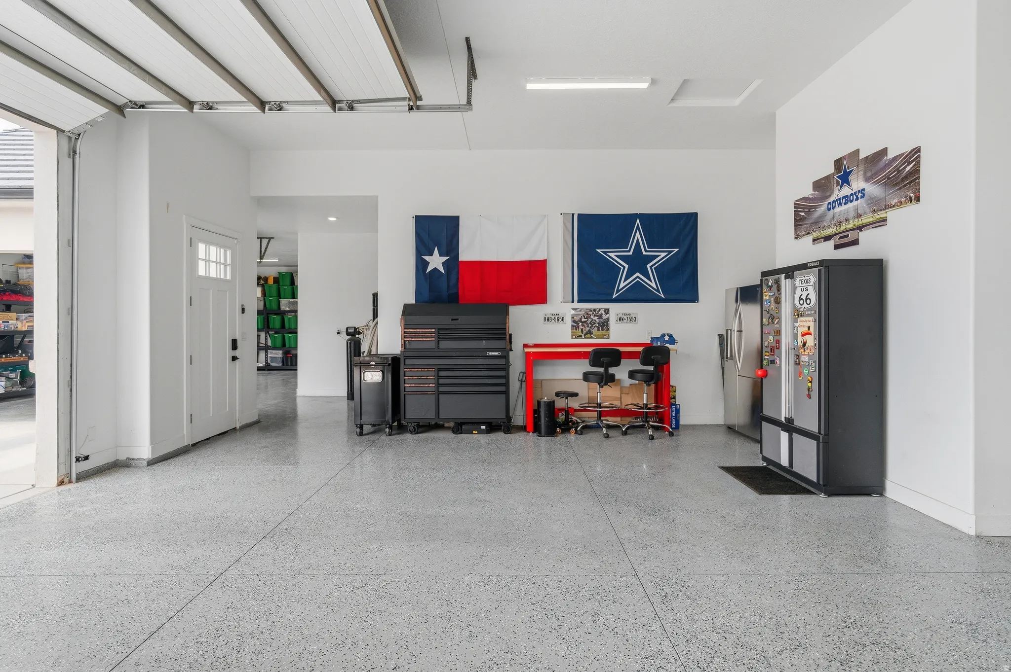 Spacious garage featuring a durable epoxy floor, white walls, overhead garage door, and a white interior door with windows.