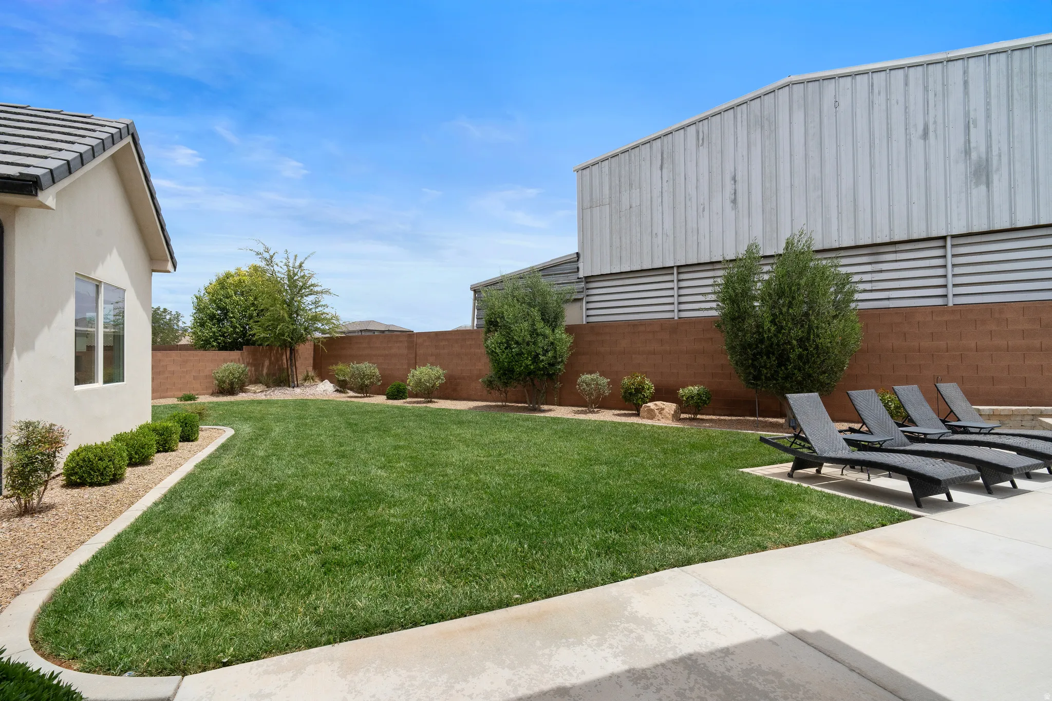 Expansive green lawn with mature landscaping, a concrete patio, and a block wall perimeter.