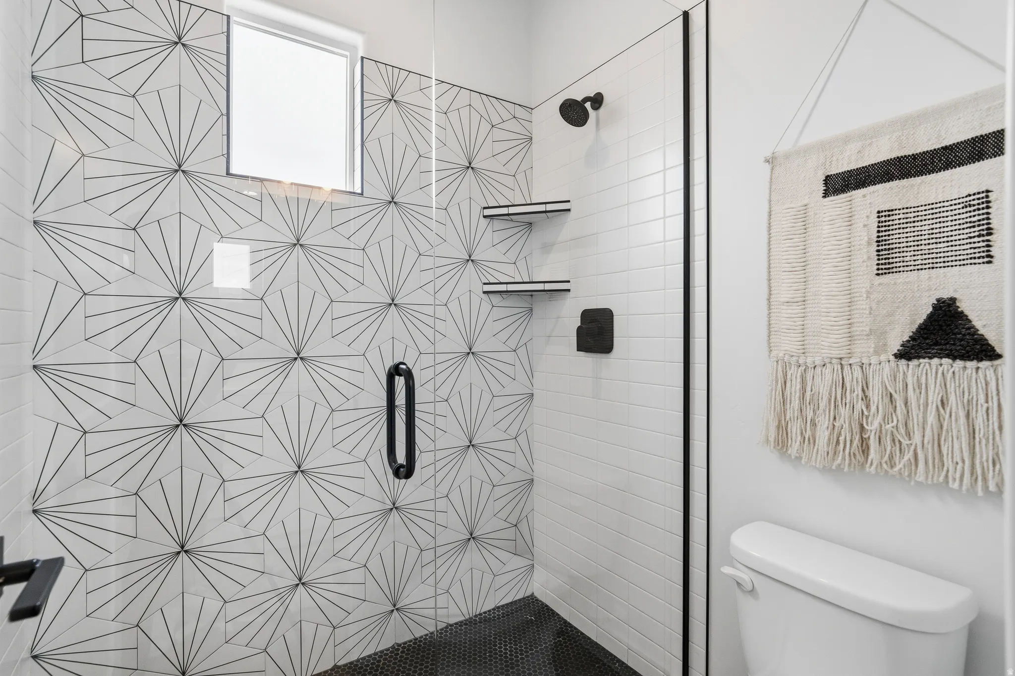 Walk-in shower with geometric patterned tile accent wall, black hexagonal floor tile, and matte black fixtures.