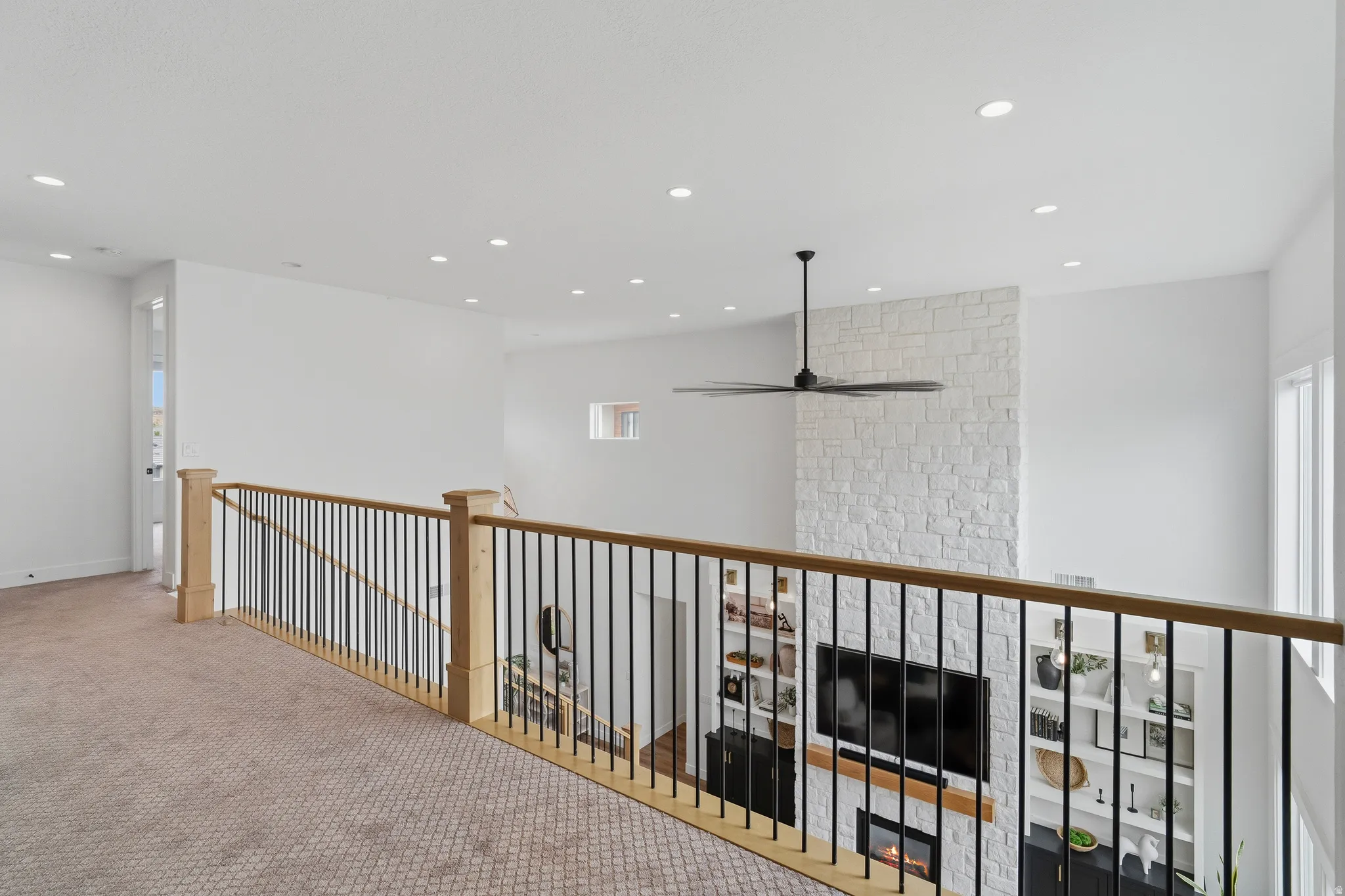 Upper-level hallway with patterned carpet flooring, natural wood handrails, and black metal balusters.