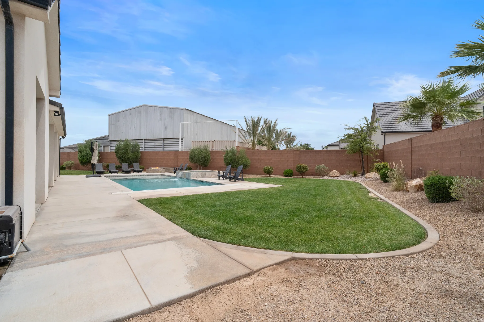 Expansive backyard featuring a rectangular swimming pool with integrated spa, a concrete patio surround, a manicured lawn area, and decorative gravel landscaping.