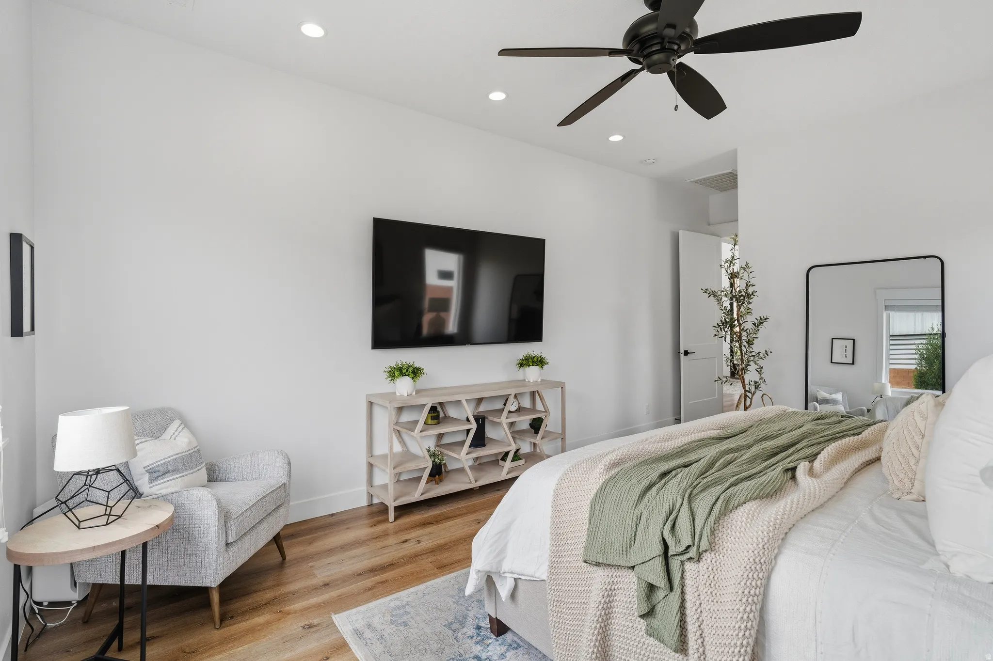 Spacious bedroom featuring light wood-finish flooring, recessed lighting, and a modern ceiling fan.