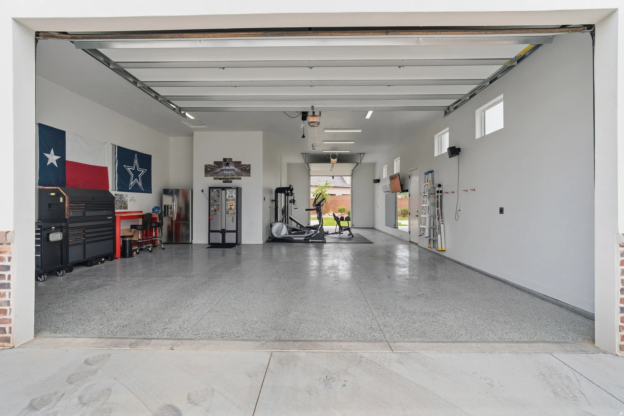 Spacious garage featuring a durable epoxy floor, multiple windows for natural light, and a brick-finish entry.
