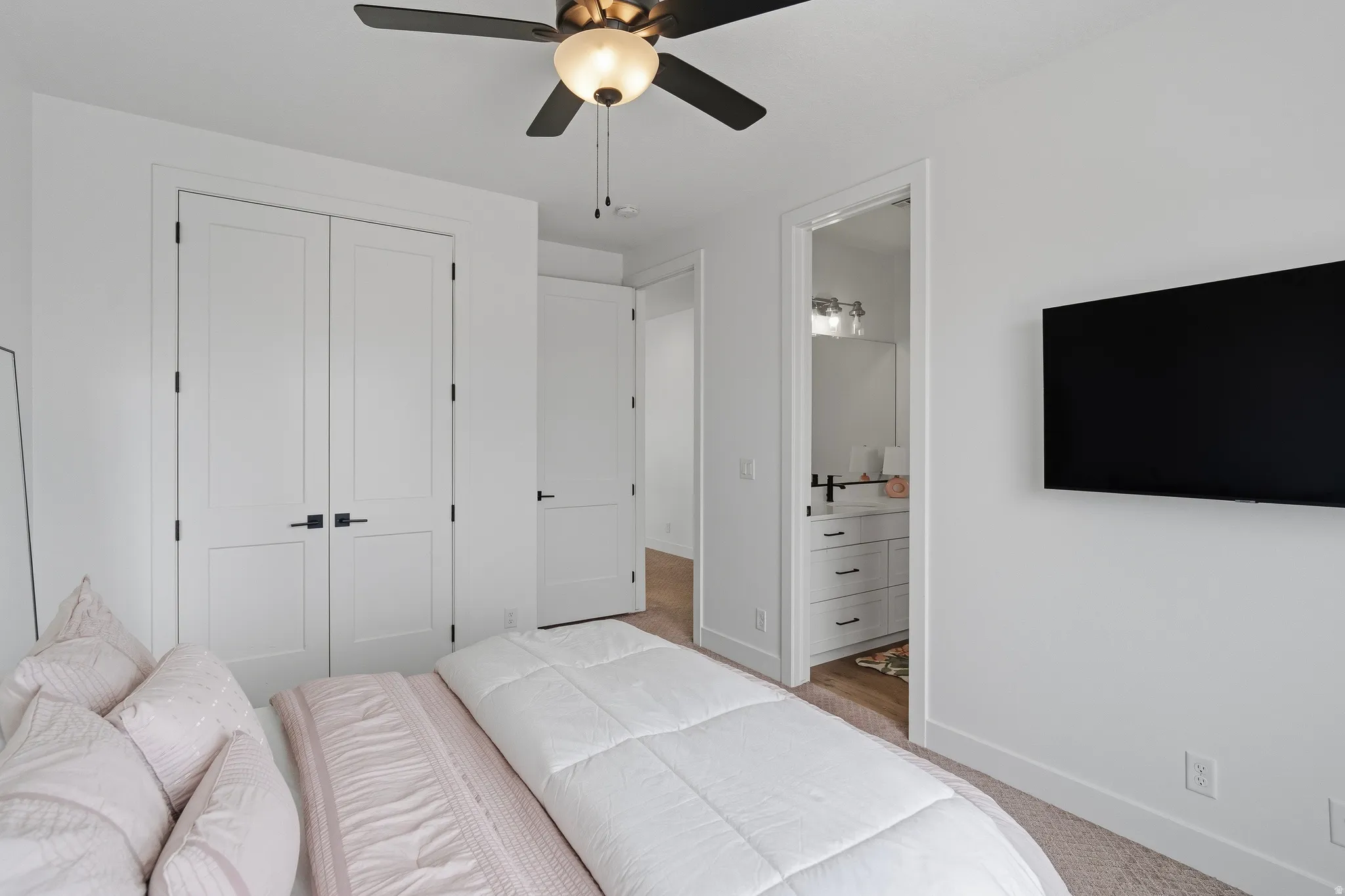 Carpeted bedroom with white walls, a ceiling fan with light fixture, and matte black hardware on doors.