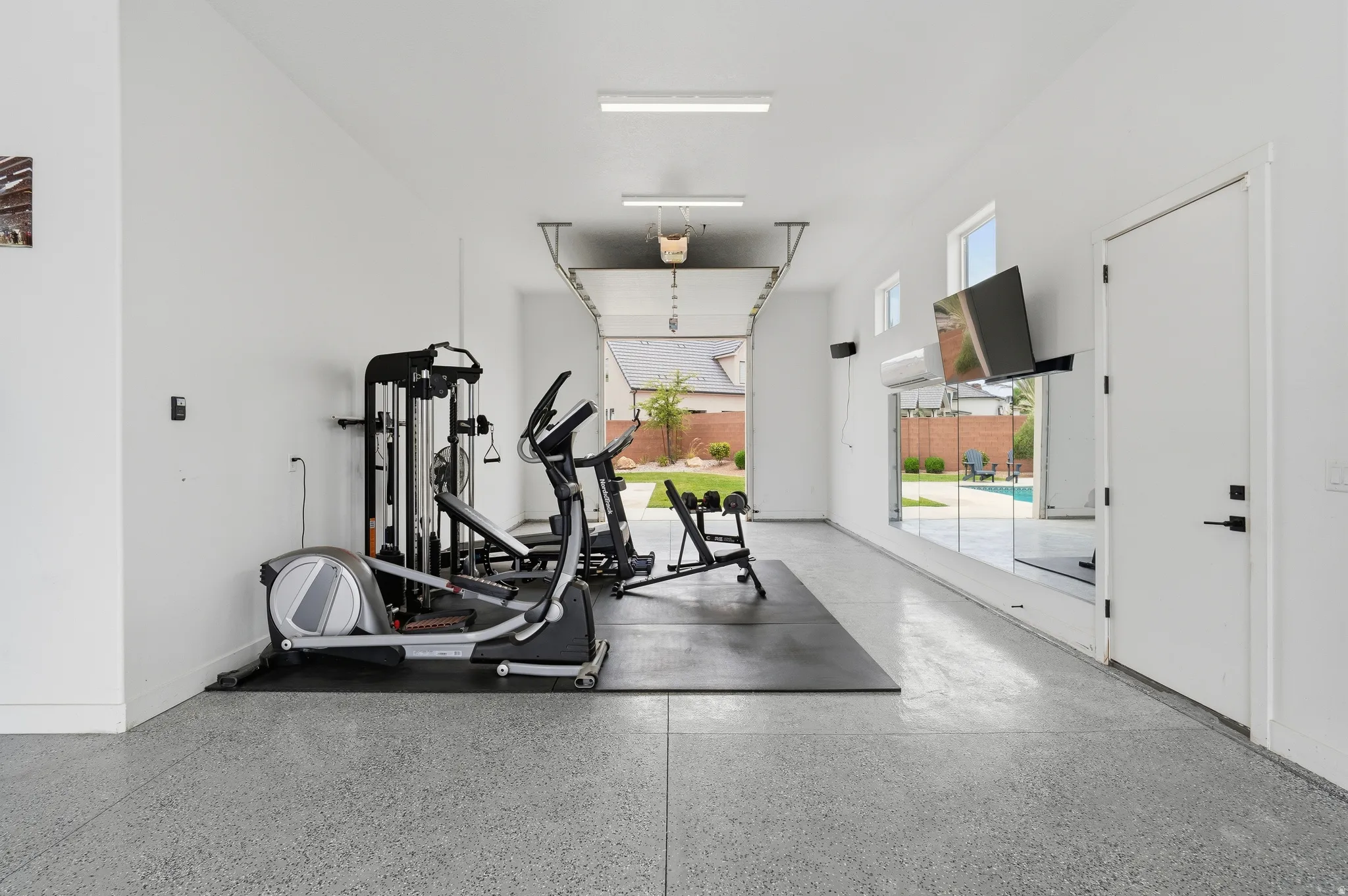 Spacious garage conversion featuring a smooth epoxy floor, white painted walls, and overhead fluorescent lighting.