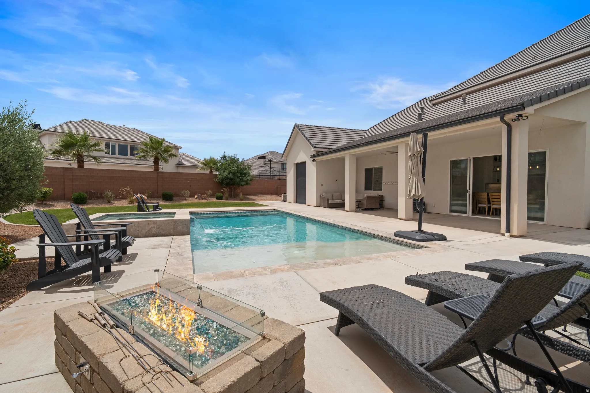 Private backyard oasis featuring a rectangular swimming pool with integrated spa, a paved patio, and a built-in stone fire pit.