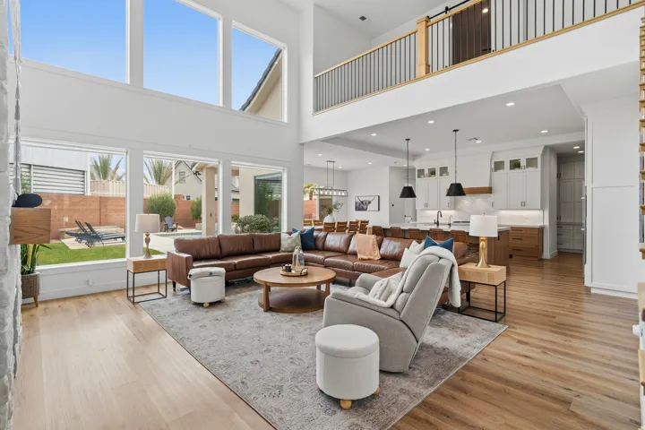 Double-height living space featuring expansive windows, wood-finish flooring, and a modern kitchen with pendant lighting and built-in cabinetry.