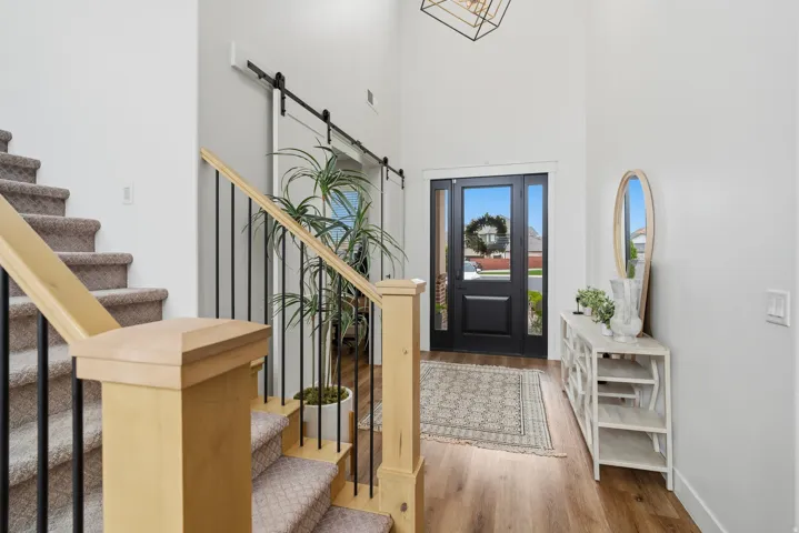 Foyer featuring a tall ceiling, wood-finish flooring, a dark entry door with glass panels, and a contrasting light wood staircase with black metal balusters.