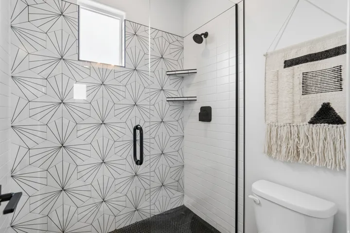Walk-in shower with geometric patterned tile accent wall, black hexagonal floor tile, and matte black fixtures.