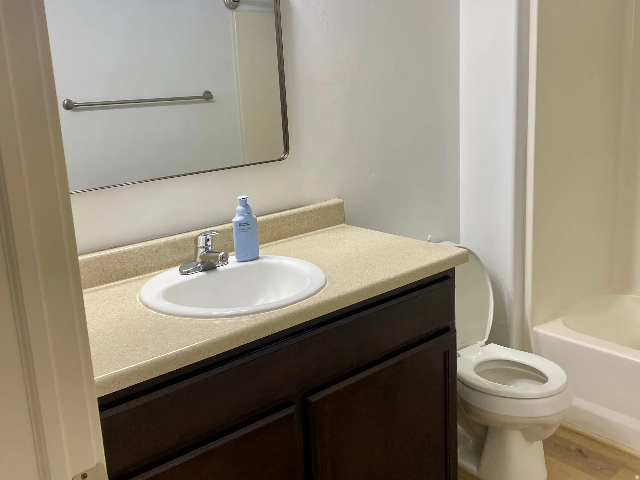 Bathroom featuring a dark wood-finish vanity with a single basin sink and neutral countertop, a rectangular mirror, and a three-light fixture