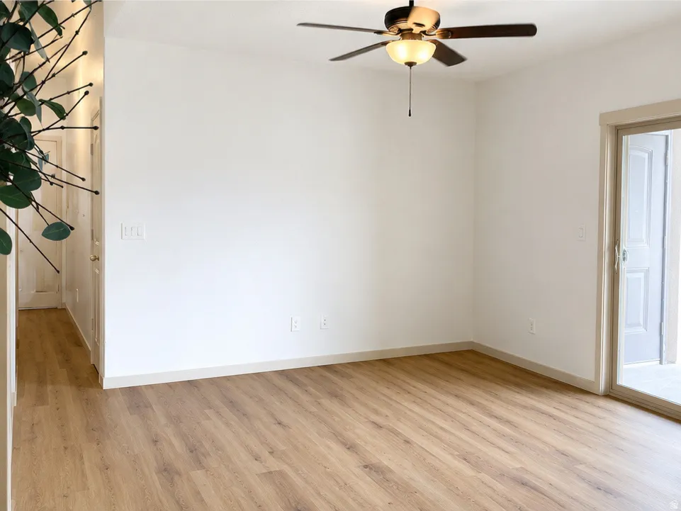Spacious room featuring wood-finish flooring, a ceiling fan with integrated lighting, and a sliding glass door providing direct outdoor access