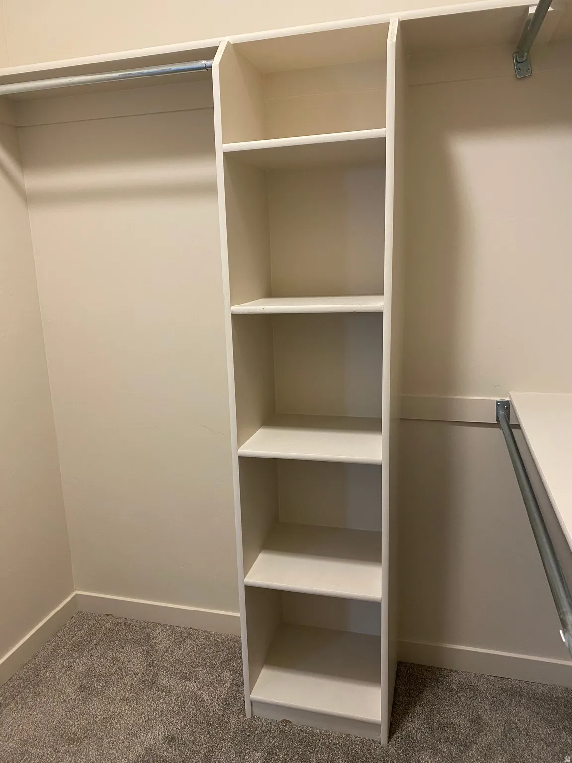 Closet organization system featuring a built-in shelving unit with five open shelves, a metal hanging rod, and neutral-toned carpeting