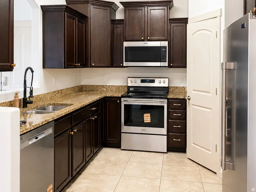 Kitchen featuring dark wood cabinetry, granite countertops, stainless steel appliances, a double basin sink with a gooseneck faucet, and tile flooring