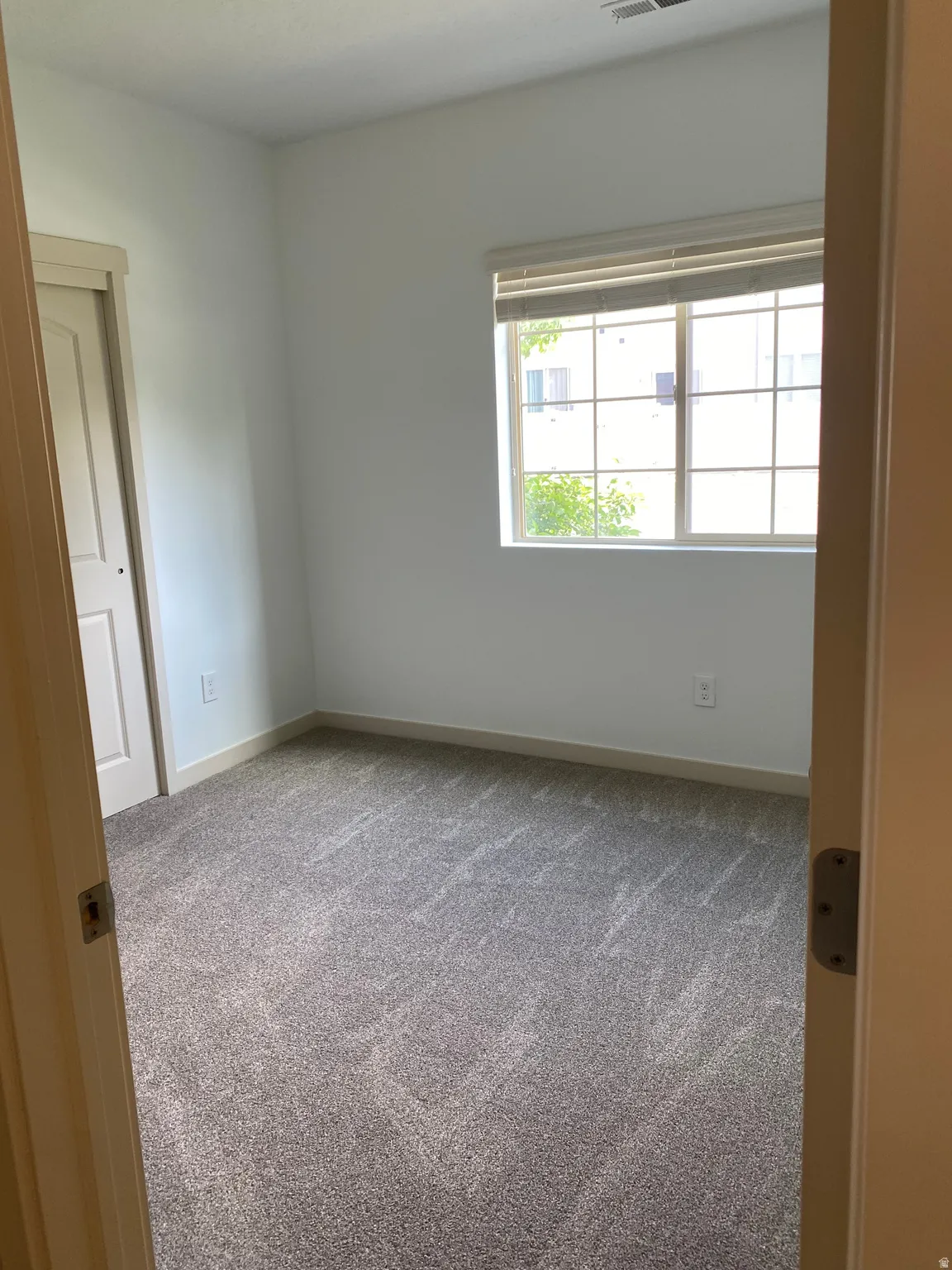 Carpeted room featuring a white interior, baseboard trim, a window with horizontal blinds, and a bi-fold closet door
