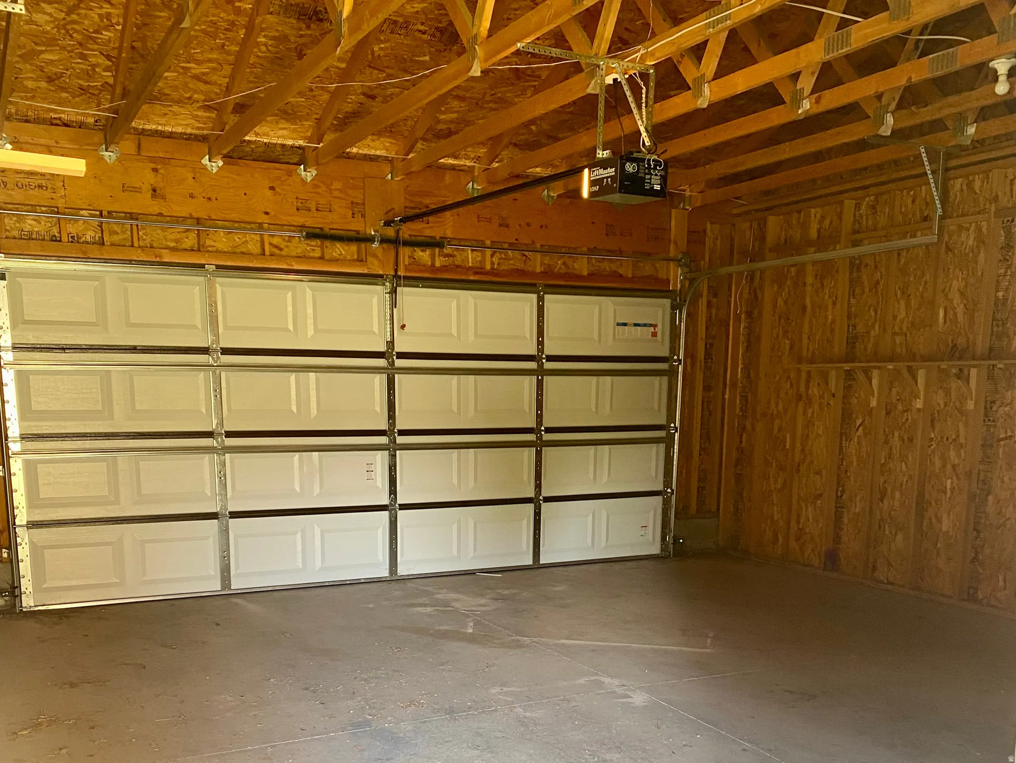 Spacious garage featuring a concrete floor, exposed wood ceiling trusses, and three individual overhead doors