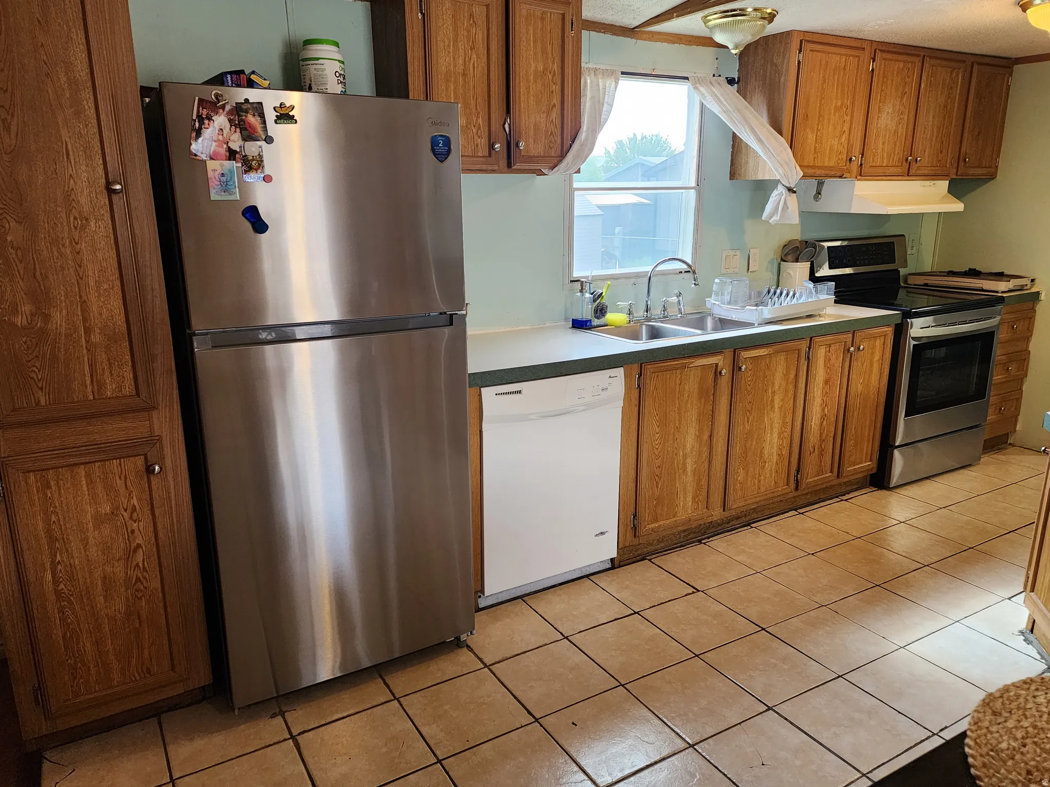 Kitchen featuring stainless steel appliances, wood-finish cabinetry, a double basin sink, and tile flooring