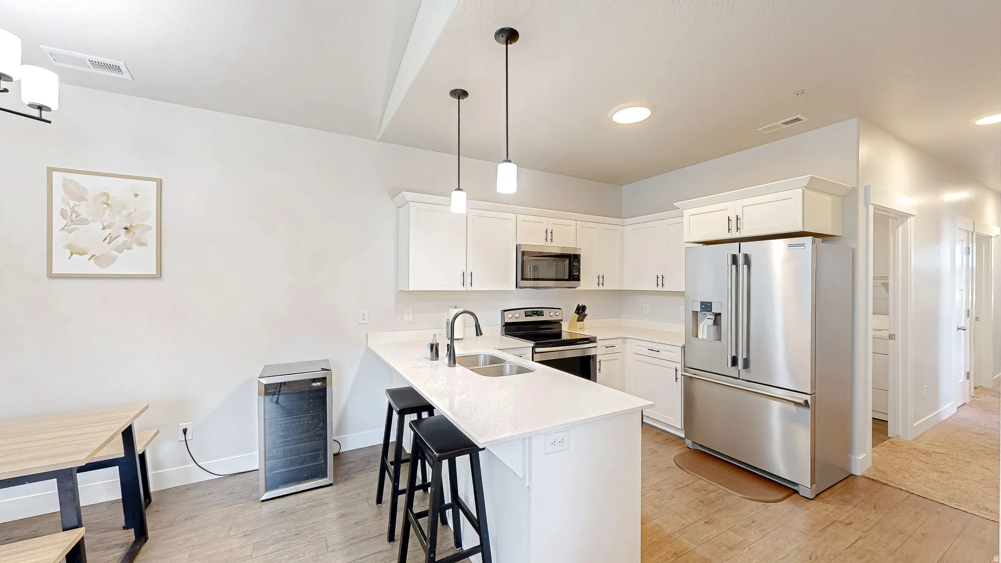 Modern kitchen featuring white shaker-style cabinetry, a central island with countertop seating, stainless steel appliances, and pendant lighting
