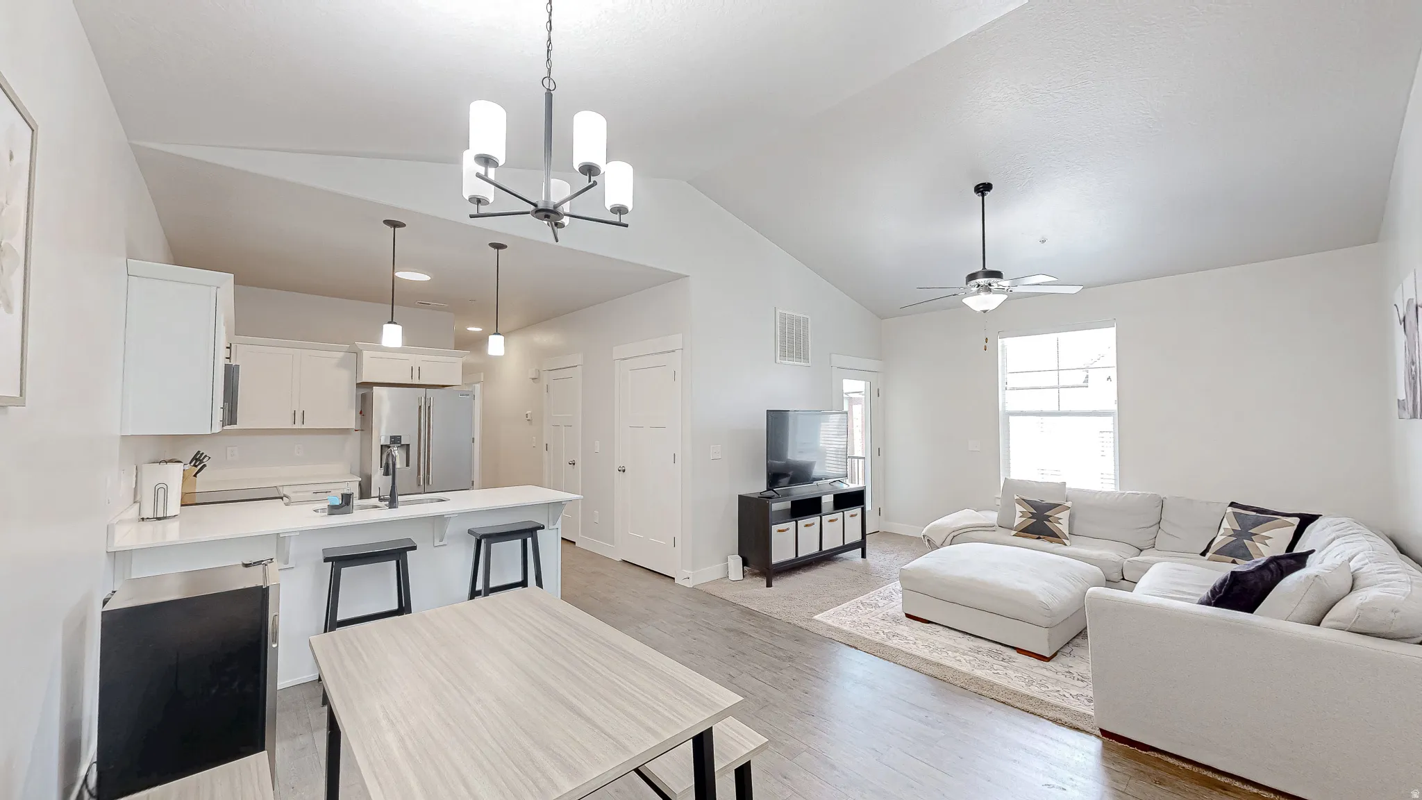 Open-concept living area featuring vaulted ceilings, wood-finish flooring, a kitchen island with seating, pendant lighting, and stainless steel appliances