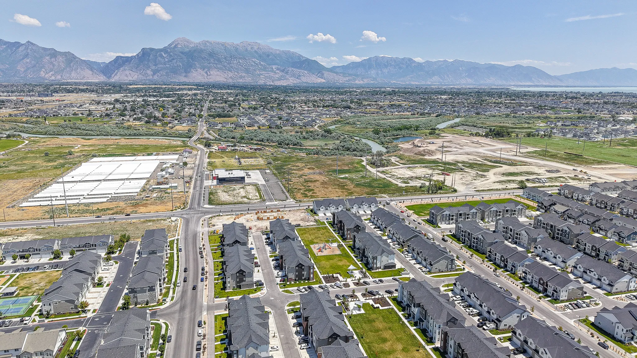 Expansive aerial view of a residential development featuring rows of townhomes and apartment buildings with dark roofs and light-colored siding
