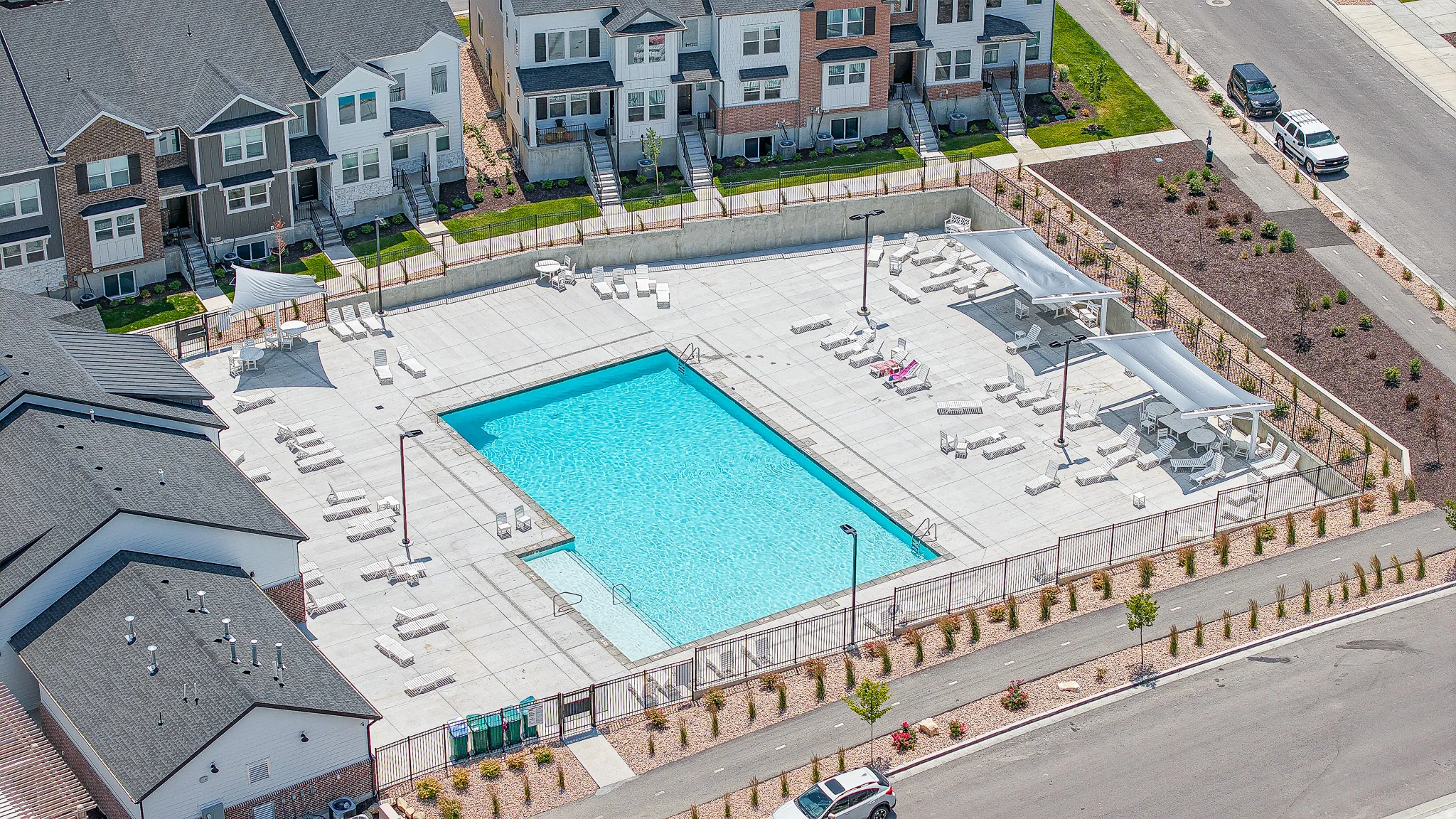 Community swimming pool with a surrounding concrete deck, lounge chairs, and shaded seating areas