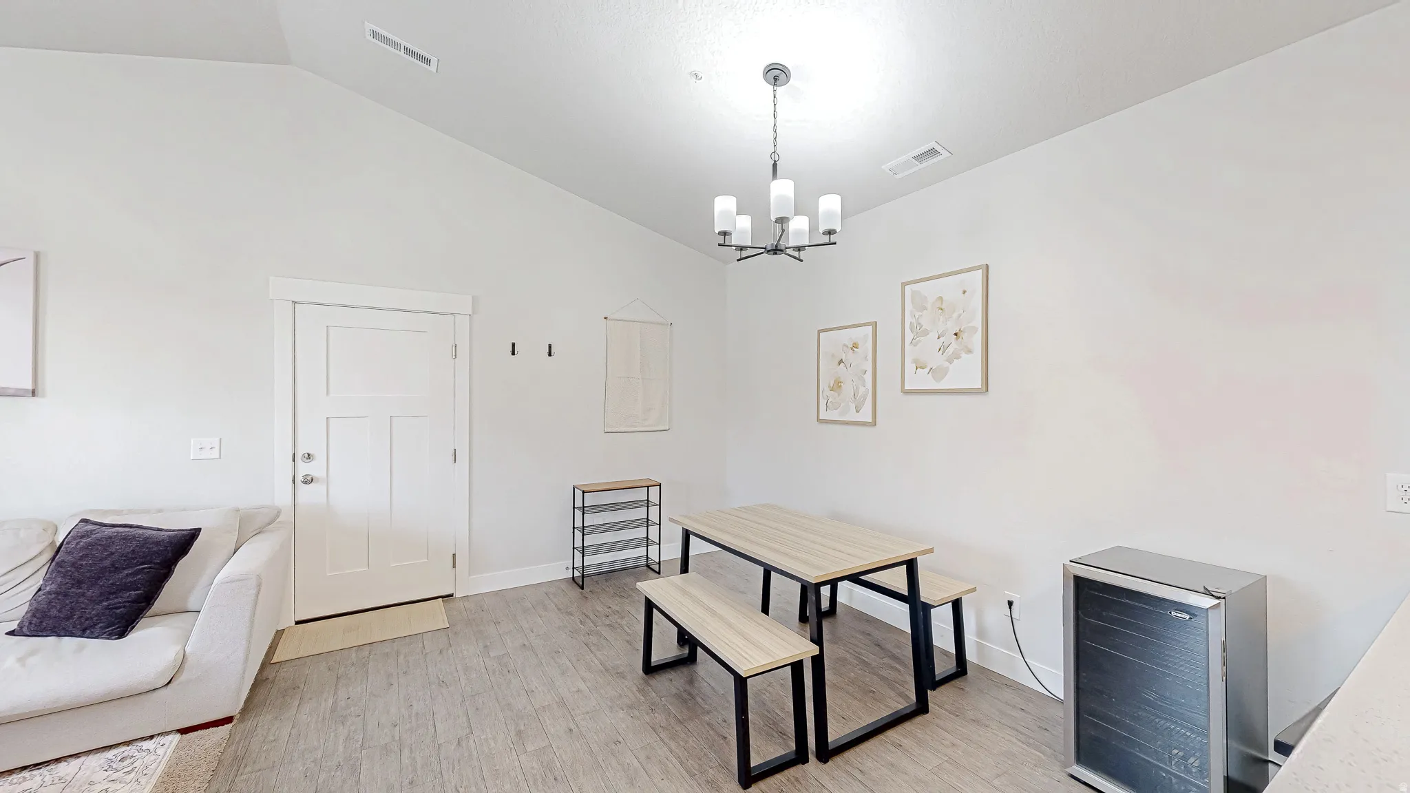 Vaulted ceiling dining area featuring wood-finish flooring, a contemporary chandelier, and a white paneled entry door