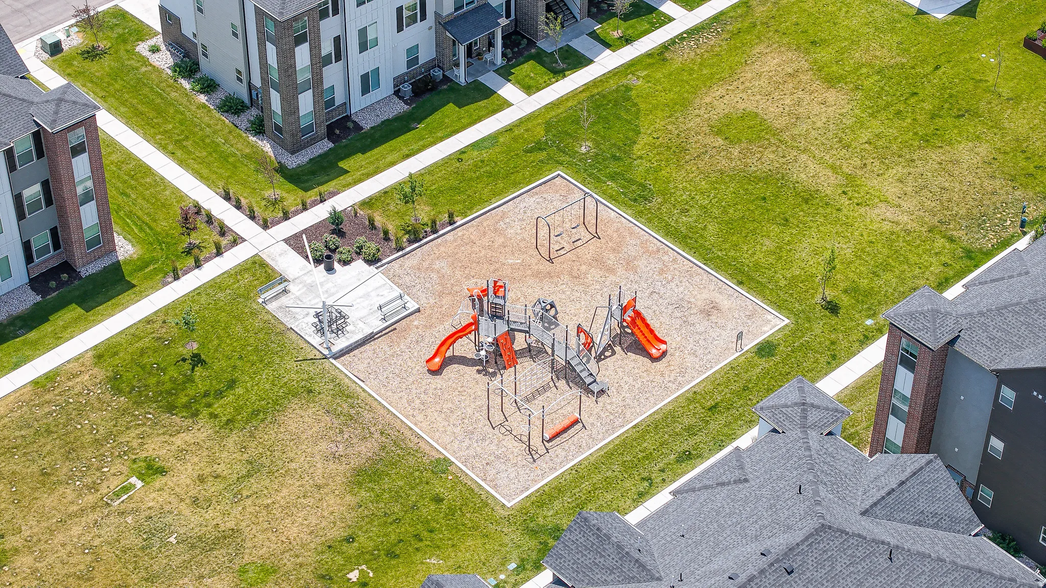 Community playground with a swing set, slides, and climbing features, surrounded by green spaces and paved pathways
