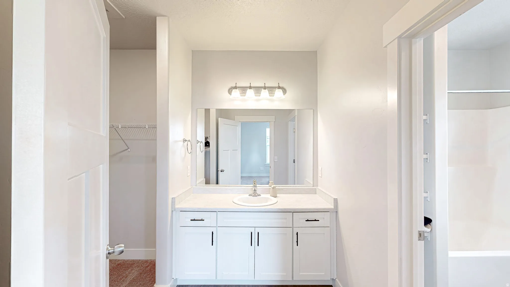 Bathroom vanity featuring a white countertop with integrated sink, white cabinetry with dark hardware, a rectangular mirror, and a four-light fixture