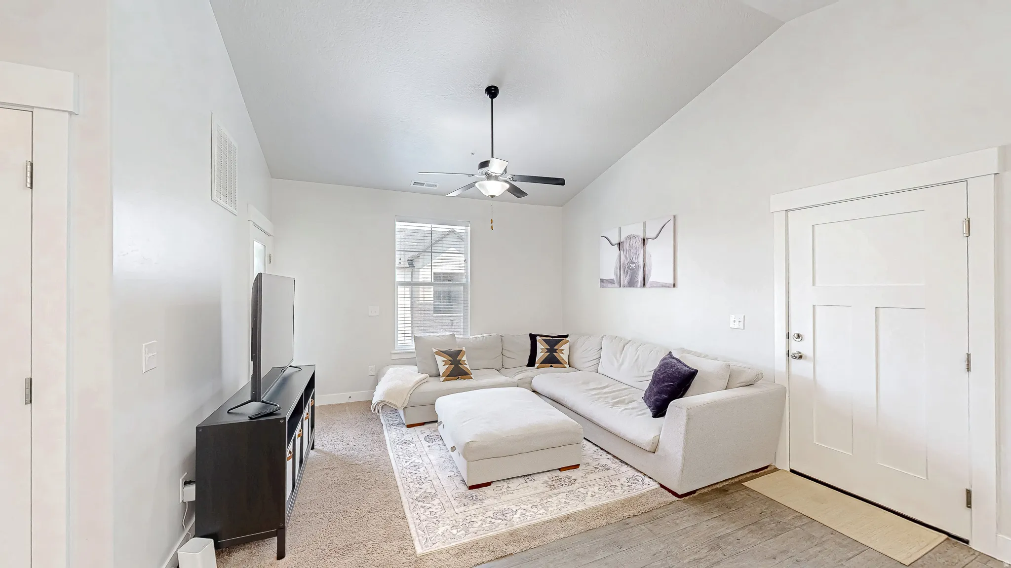 Vaulted ceiling living room featuring a ceiling fan, a multi-pane window, and a three-panel interior door