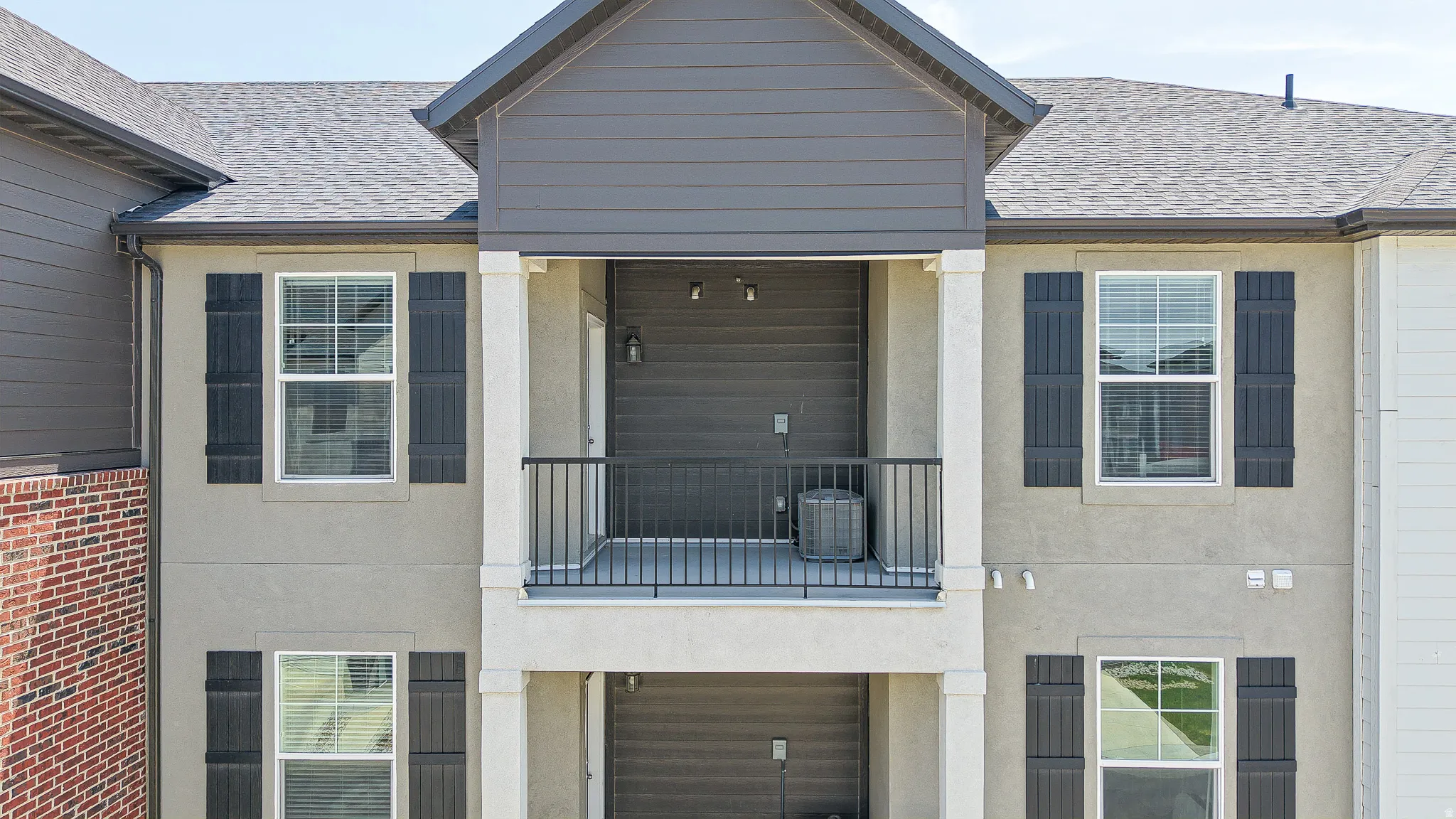 Multi-level facade featuring a covered balcony with black metal railing, stucco exterior, and dark shutters