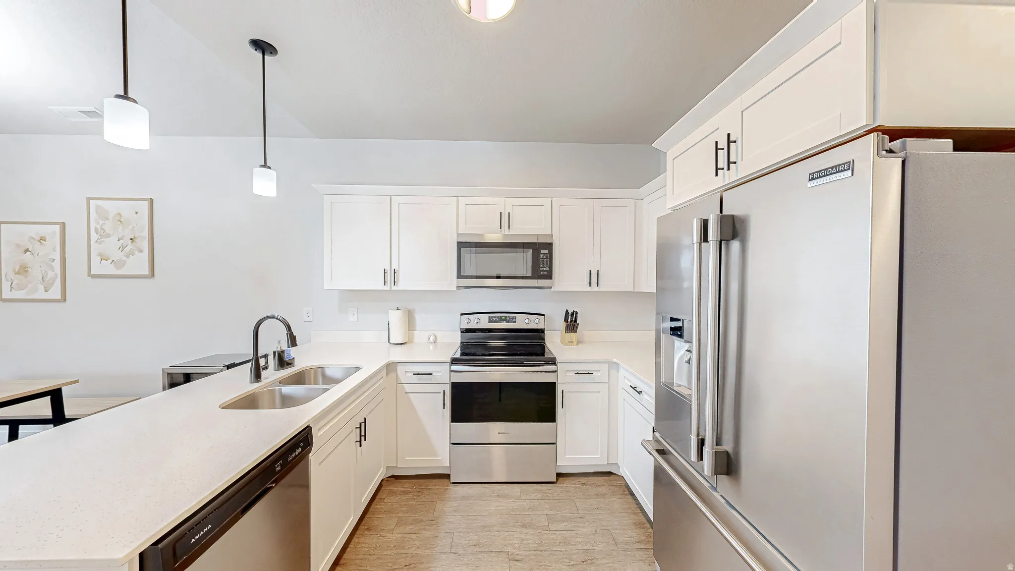 Modern kitchen featuring white cabinetry, stainless steel appliances, a double basin sink, and pendant lighting