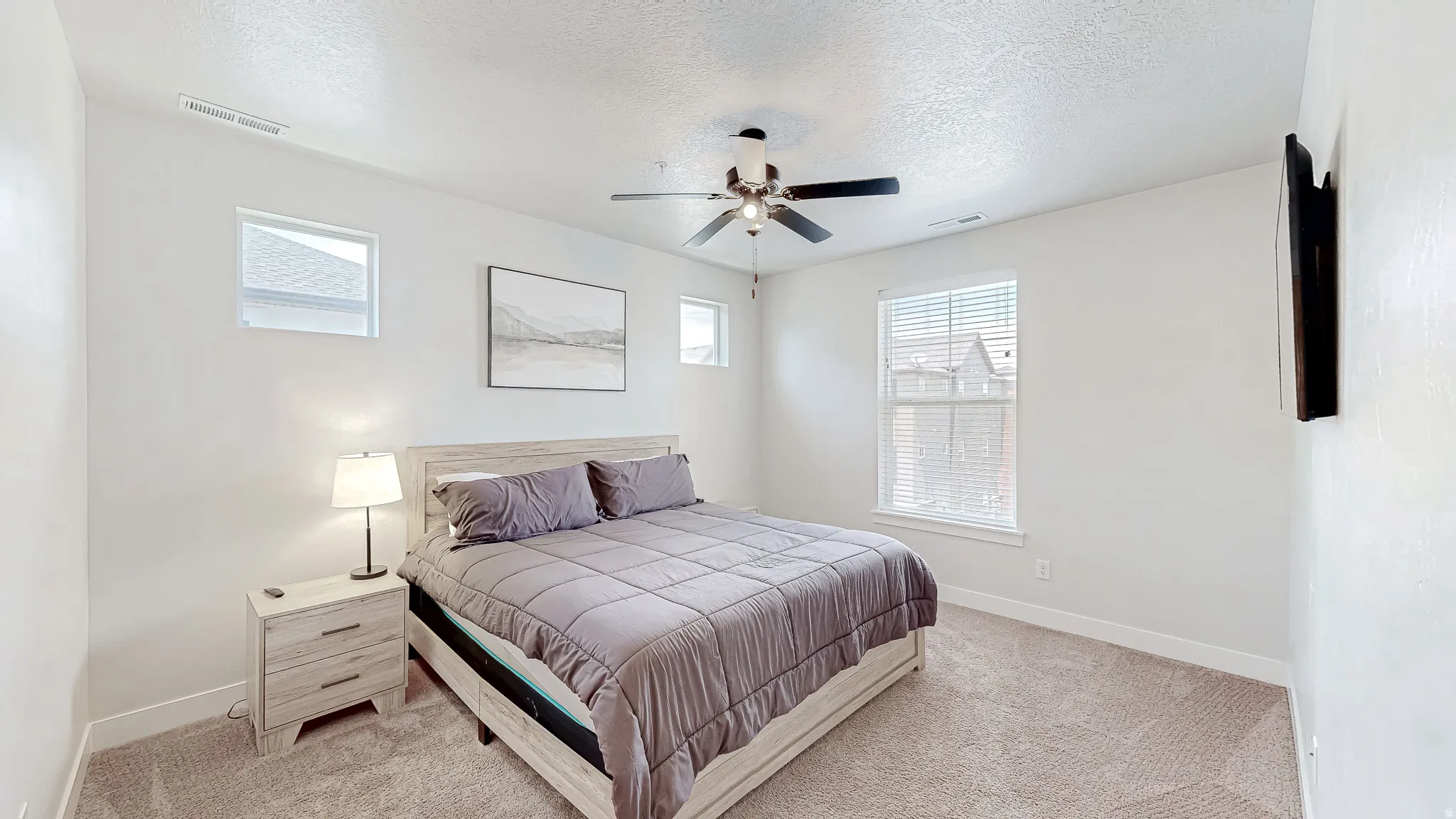 Carpeted interior space featuring a ceiling fan with integrated lighting, multiple windows with blinds, and white walls