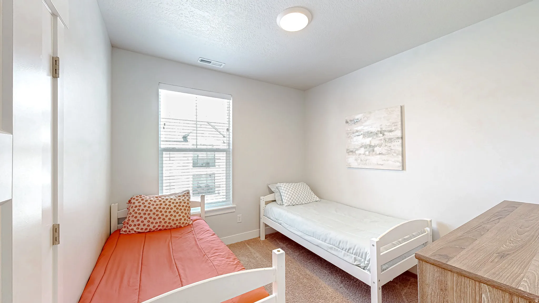 Bright interior space featuring a single window with blinds, light-colored walls, and textured carpet flooring