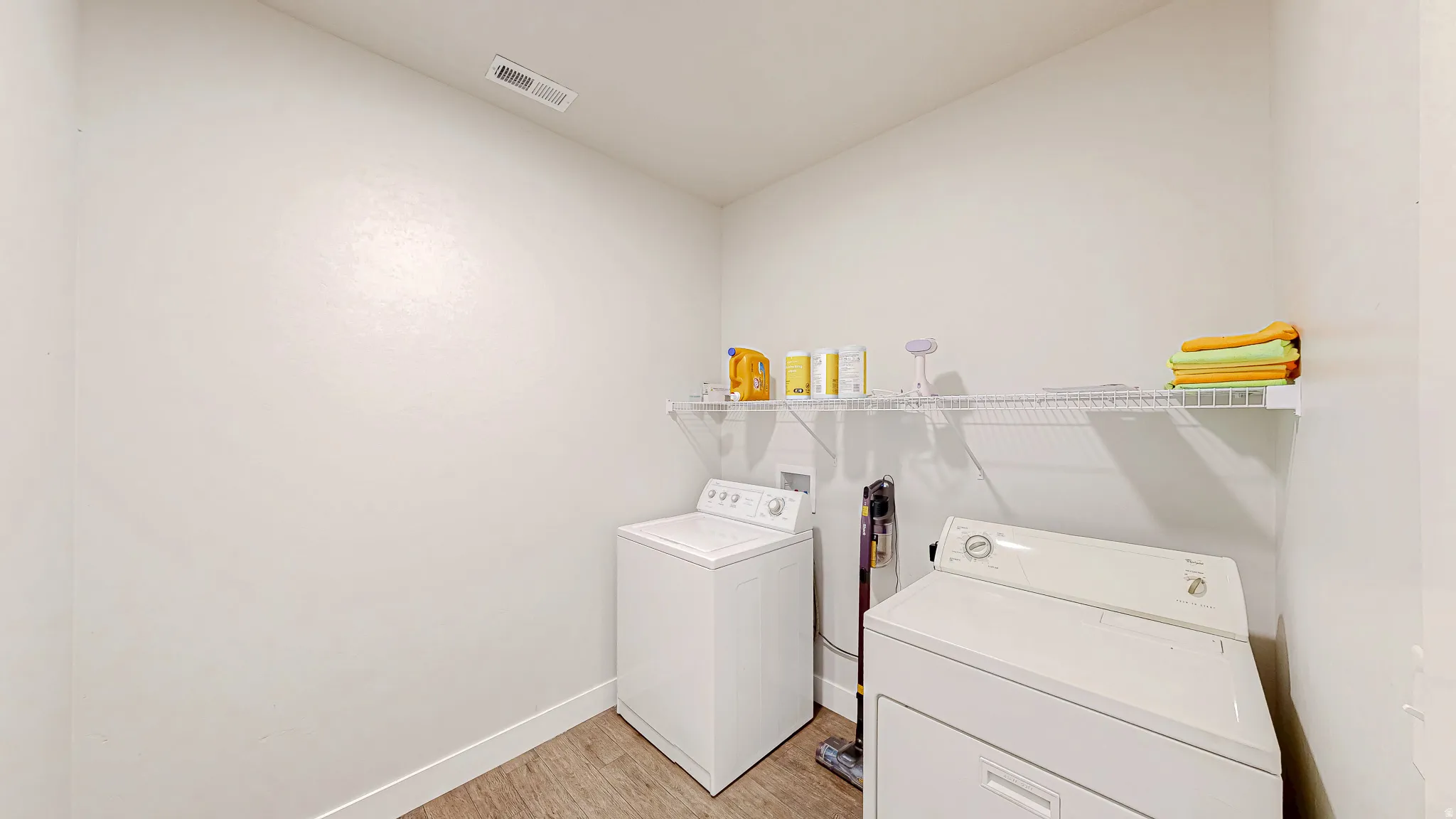 Dedicated laundry room featuring wood-finish flooring, white walls, and a recessed ceiling vent
