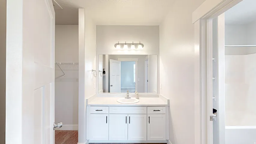 Bathroom vanity featuring a white countertop with integrated sink, white cabinetry with dark hardware, a rectangular mirror, and a four-light fixture